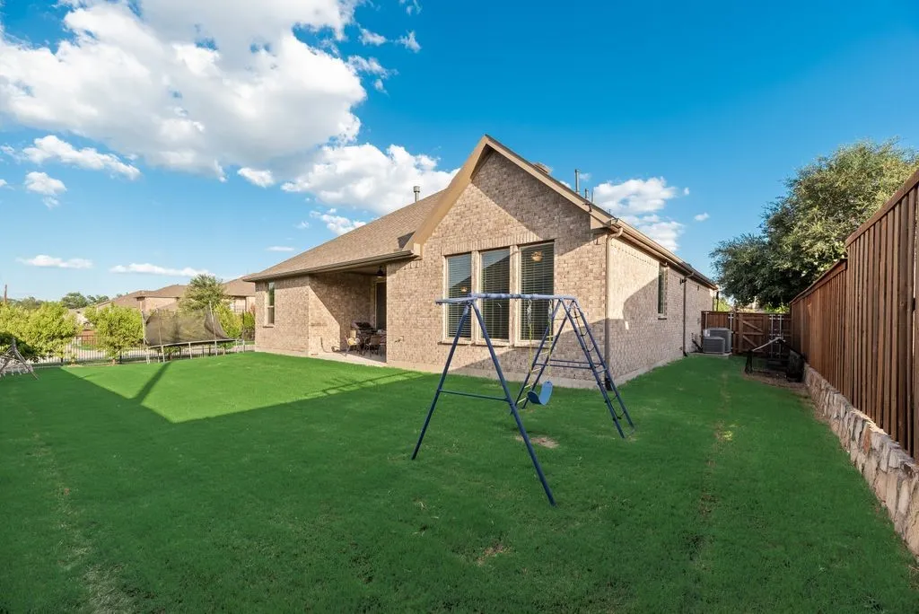 Spacious backyard featuring a lush lawn, a full brick exterior, a covered patio, a privacy fence with a stone base, and multiple windows