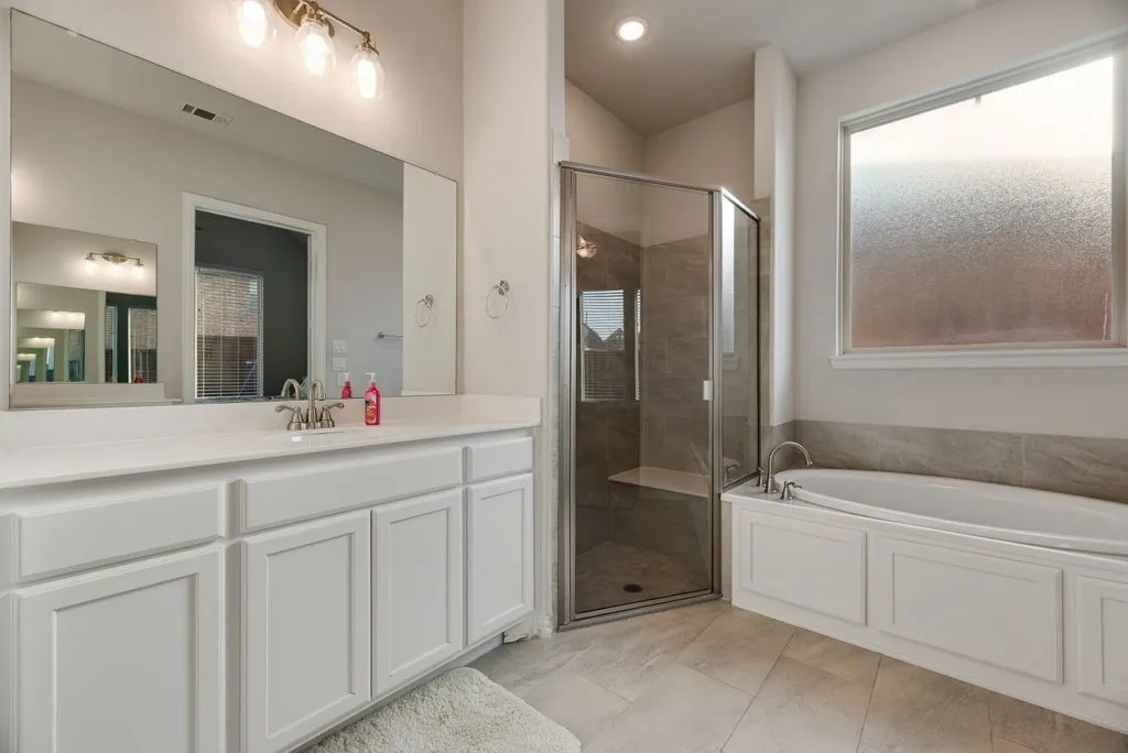 Spacious bathroom featuring a built-in tub with a tiled surround, a separate shower with glass enclosure, and a large vanity with ample storage