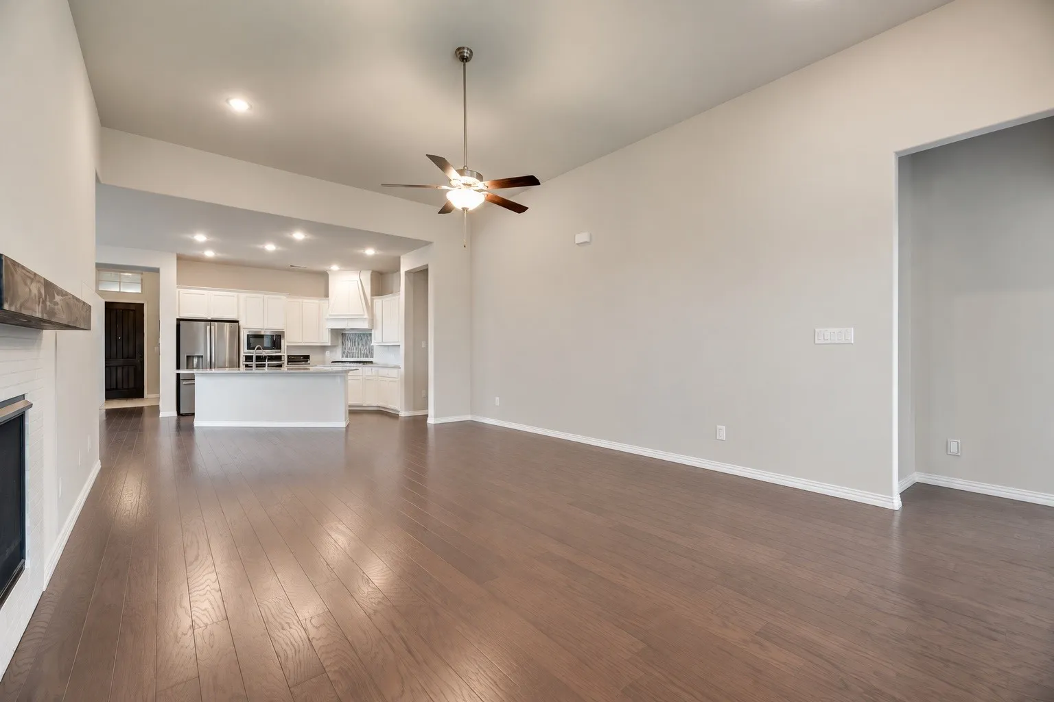 Expansive living area with wood-finish flooring, vaulted ceiling, and a ceiling fan