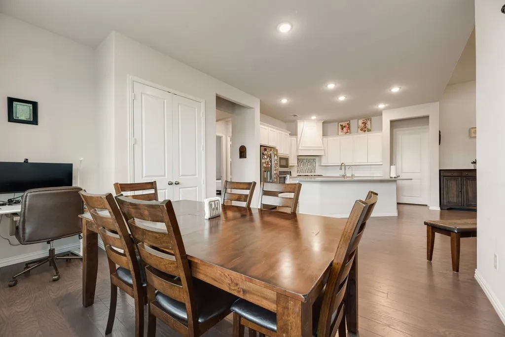 Wood-finish flooring throughout, featuring a kitchen with white cabinetry, a central island, and a tiled backsplash