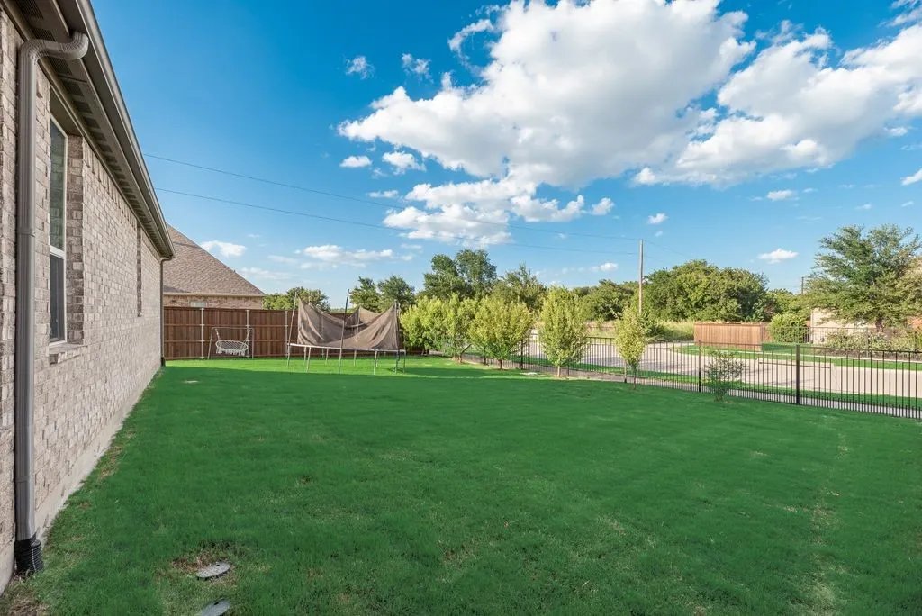 Expansive green lawn with a black wrought iron fence and mature trees