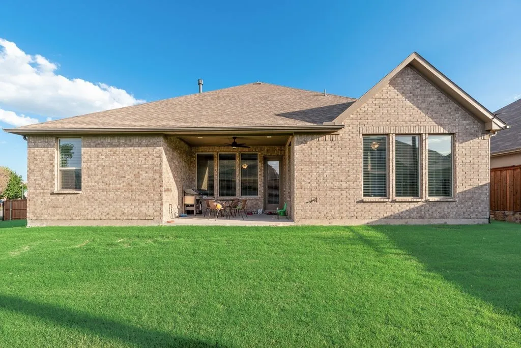 Rear exterior featuring a brick facade with a covered patio, multiple windows, and a generously sized lawn