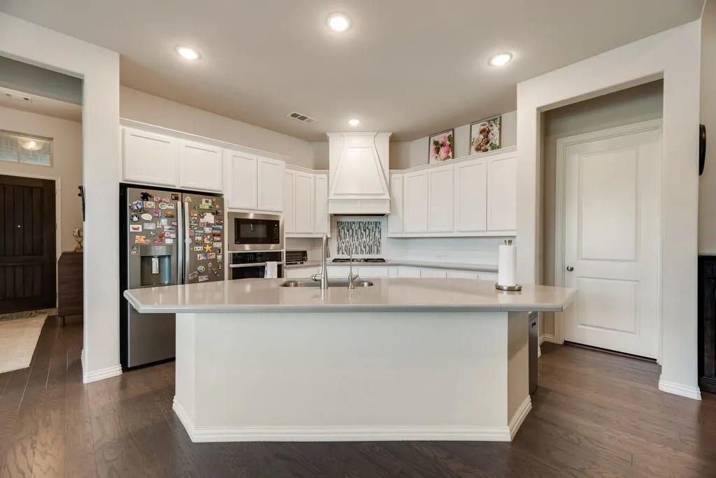Kitchen featuring an expansive island with an undermount sink, light-toned countertops, white cabinetry, stainless steel appliances, and dark wood-finish flooring