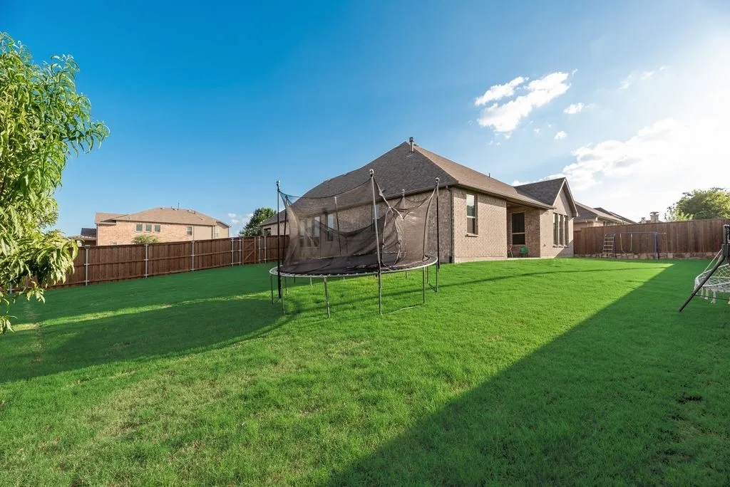 Expansive backyard featuring a lush green lawn, full wood fencing, and a brick-veneer exterior with multiple windows
