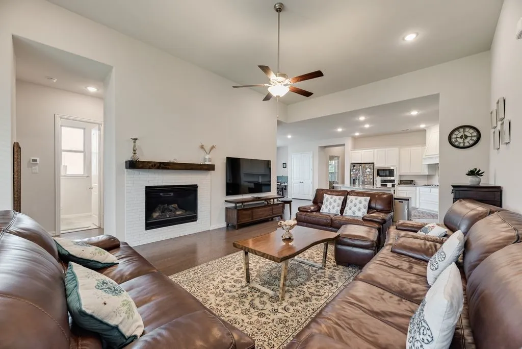 Open-concept living space featuring vaulted ceilings, wood-finish flooring, a white brick fireplace with a wood mantle, and recessed lighting