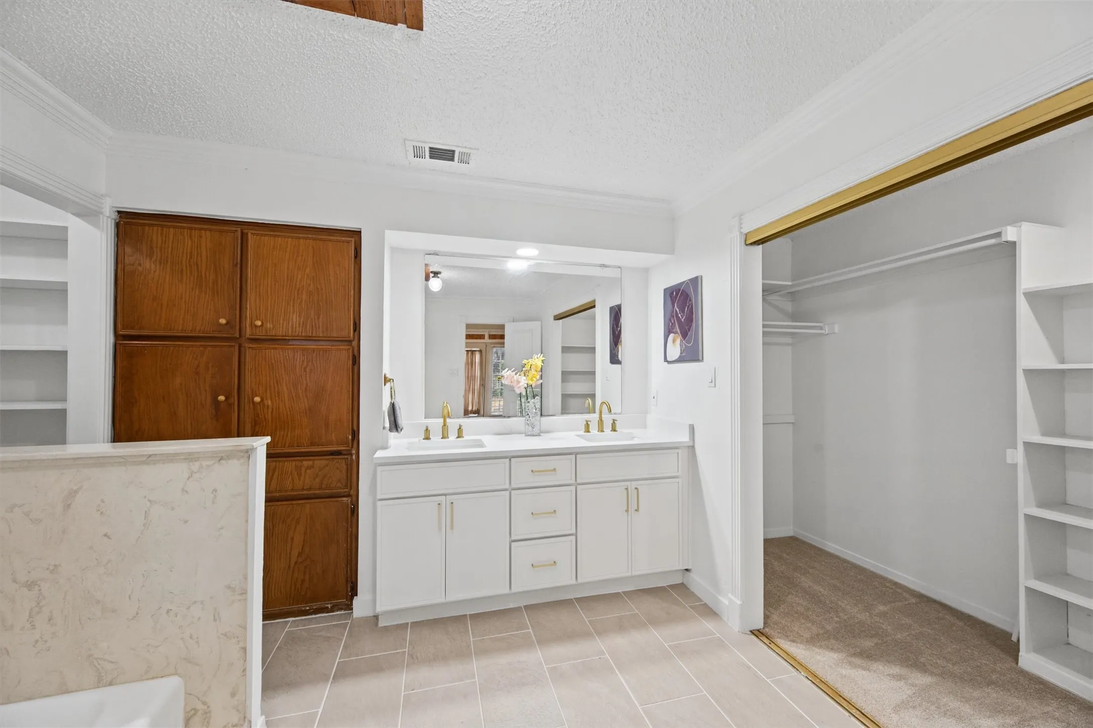 Dual vanity with gold-finish faucets and hardware, built-in wooden cabinetry, recessed lighting, and a walk-in closet with built-in shelving