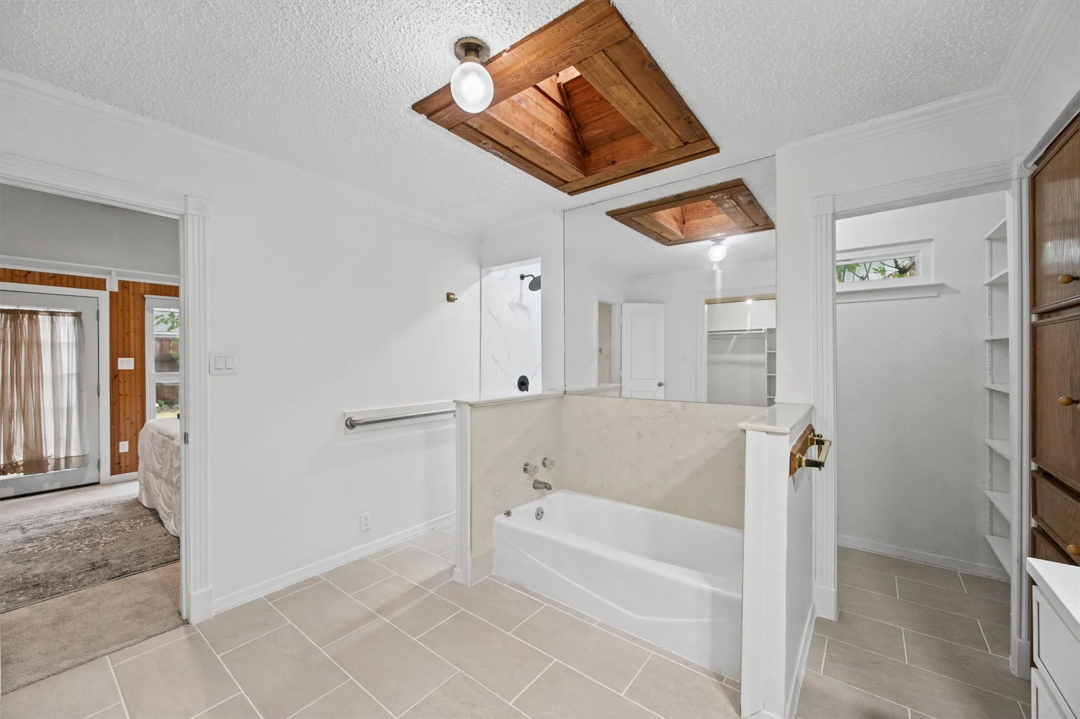 White soaking tub with light-toned surround, tiled flooring, wood-finish built-in cabinetry, and integrated shelving