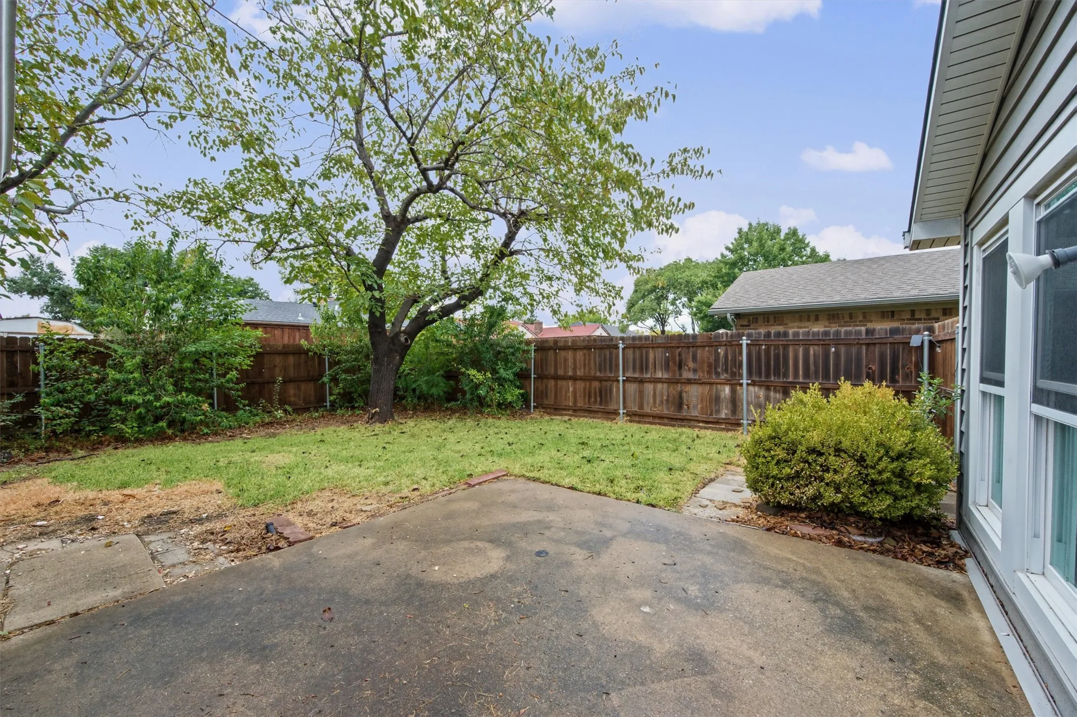 Expansive backyard featuring a concrete patio, wood fencing, and mature trees