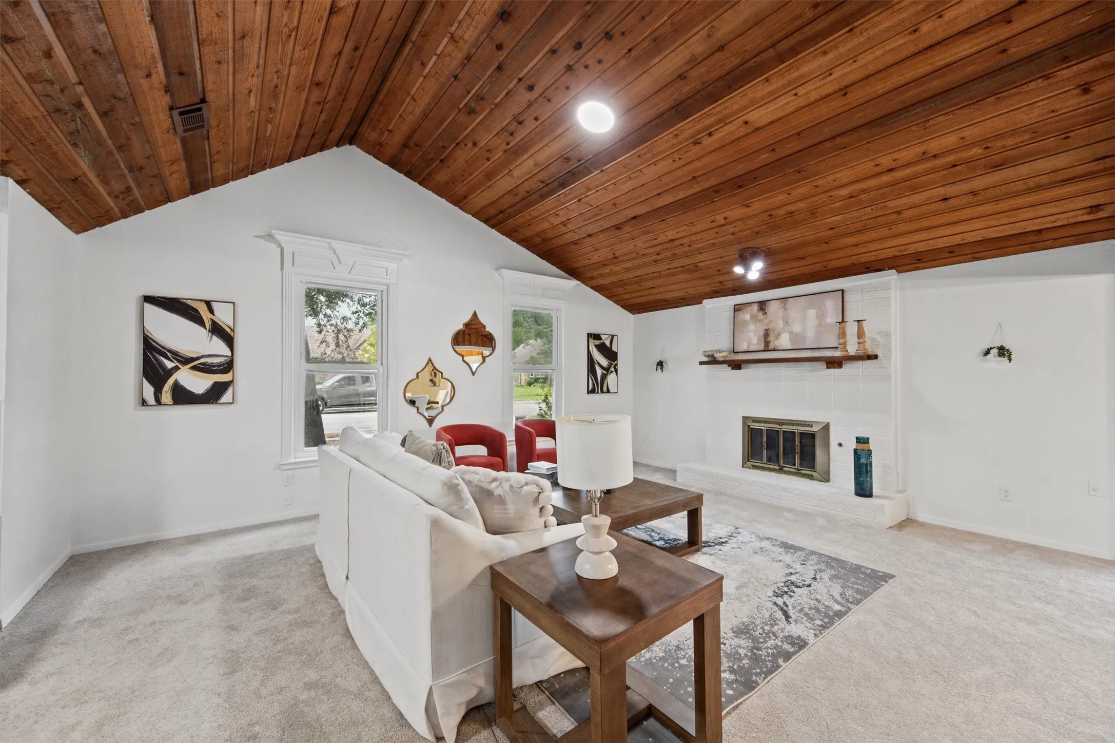 Vaulted wood-paneled ceiling, white painted brick fireplace, light-toned carpet flooring, recessed lighting, and decorative window casings