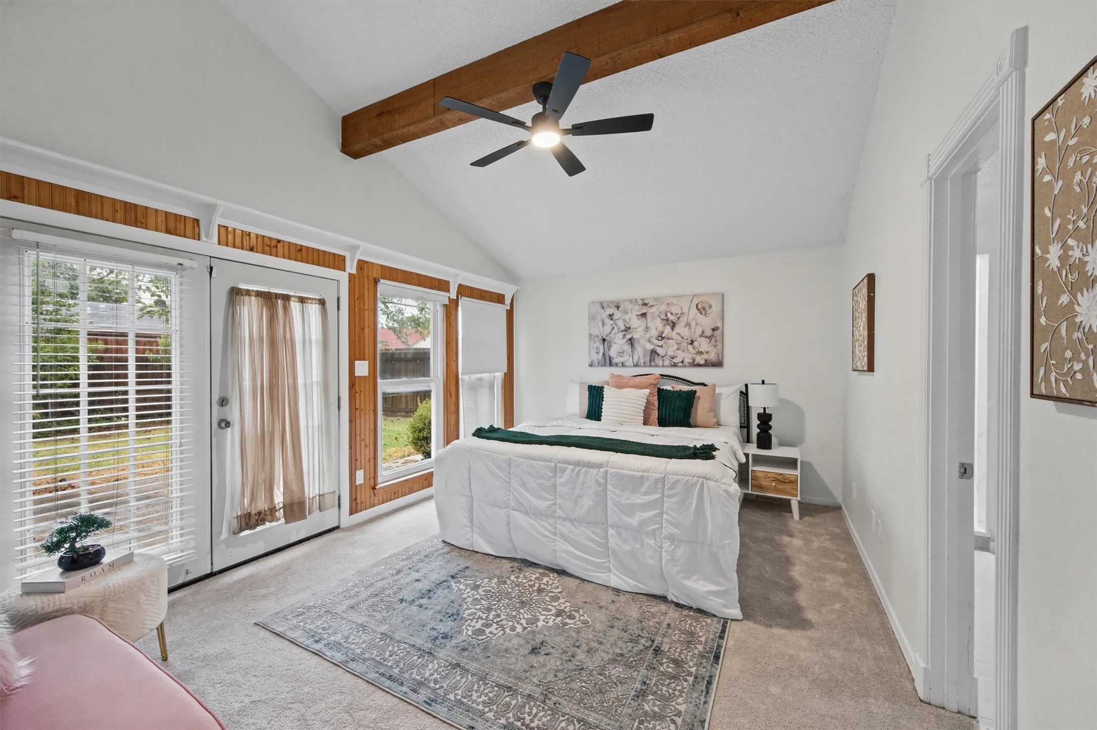 Vaulted ceiling with exposed wood beam, ceiling fan, and large windows with blinds