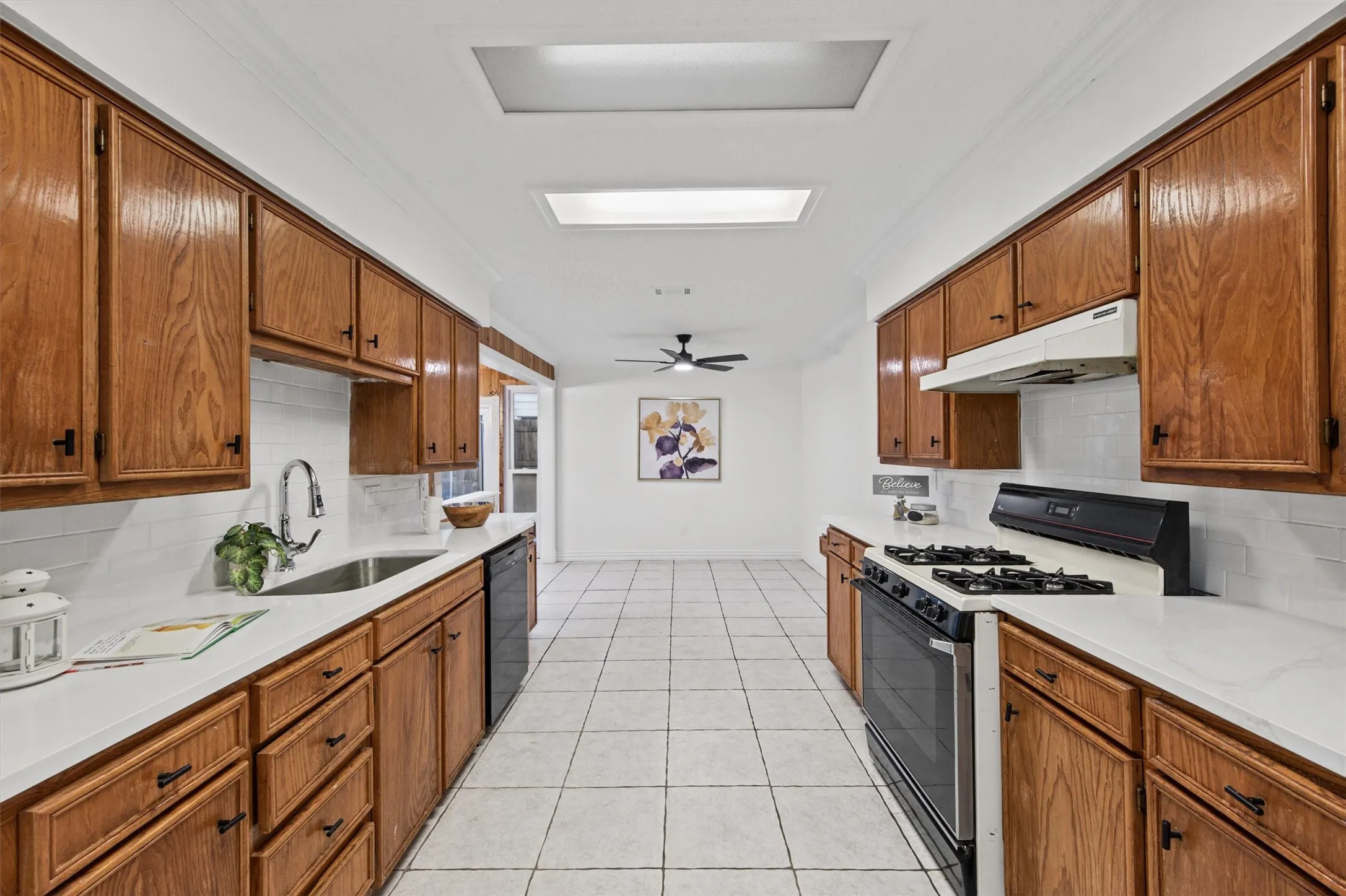 Galley kitchen featuring warm wood cabinetry throughout, white subway tile backsplash, white countertops, stainless steel gas range, and recessed ceiling lighting