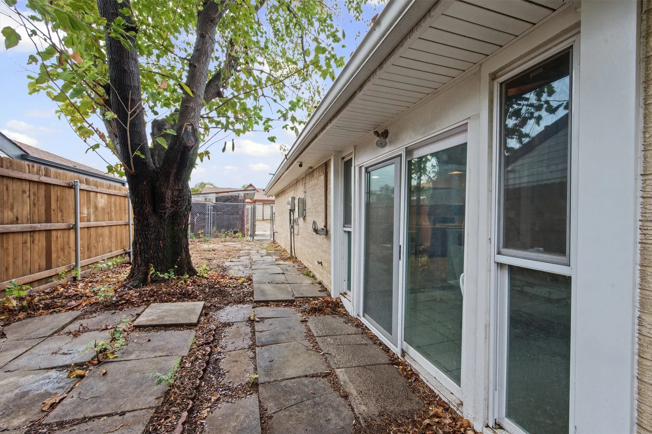 Exterior patio area featuring a mature tree, stone paver pathway, privacy fencing, and multiple sliding glass doors