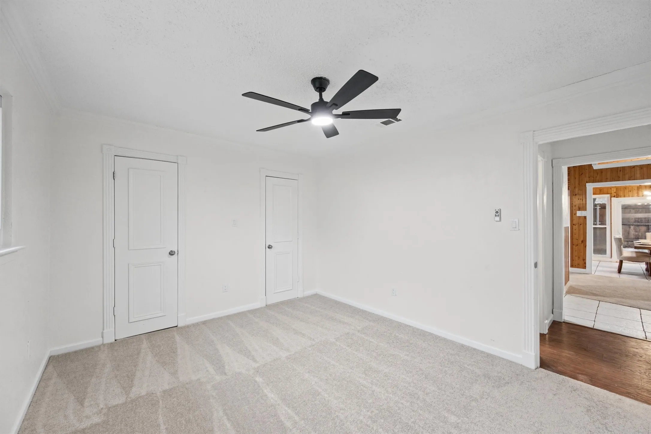 Light-toned carpeted flooring, white walls, and a modern ceiling fan with integrated lighting