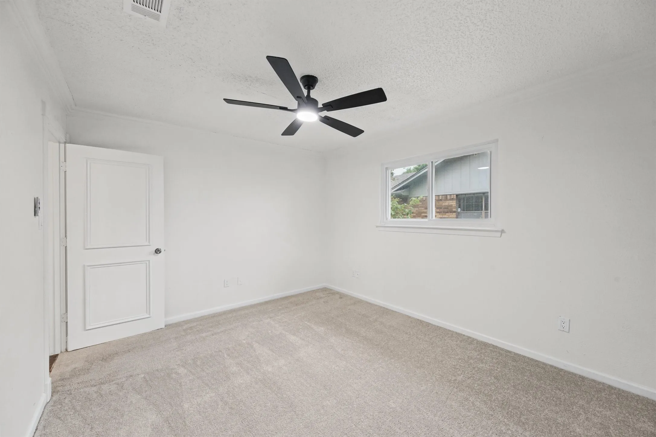 Neutral wall paint, ceiling-mounted light fixture with fan, white window trim, and light-toned carpet flooring
