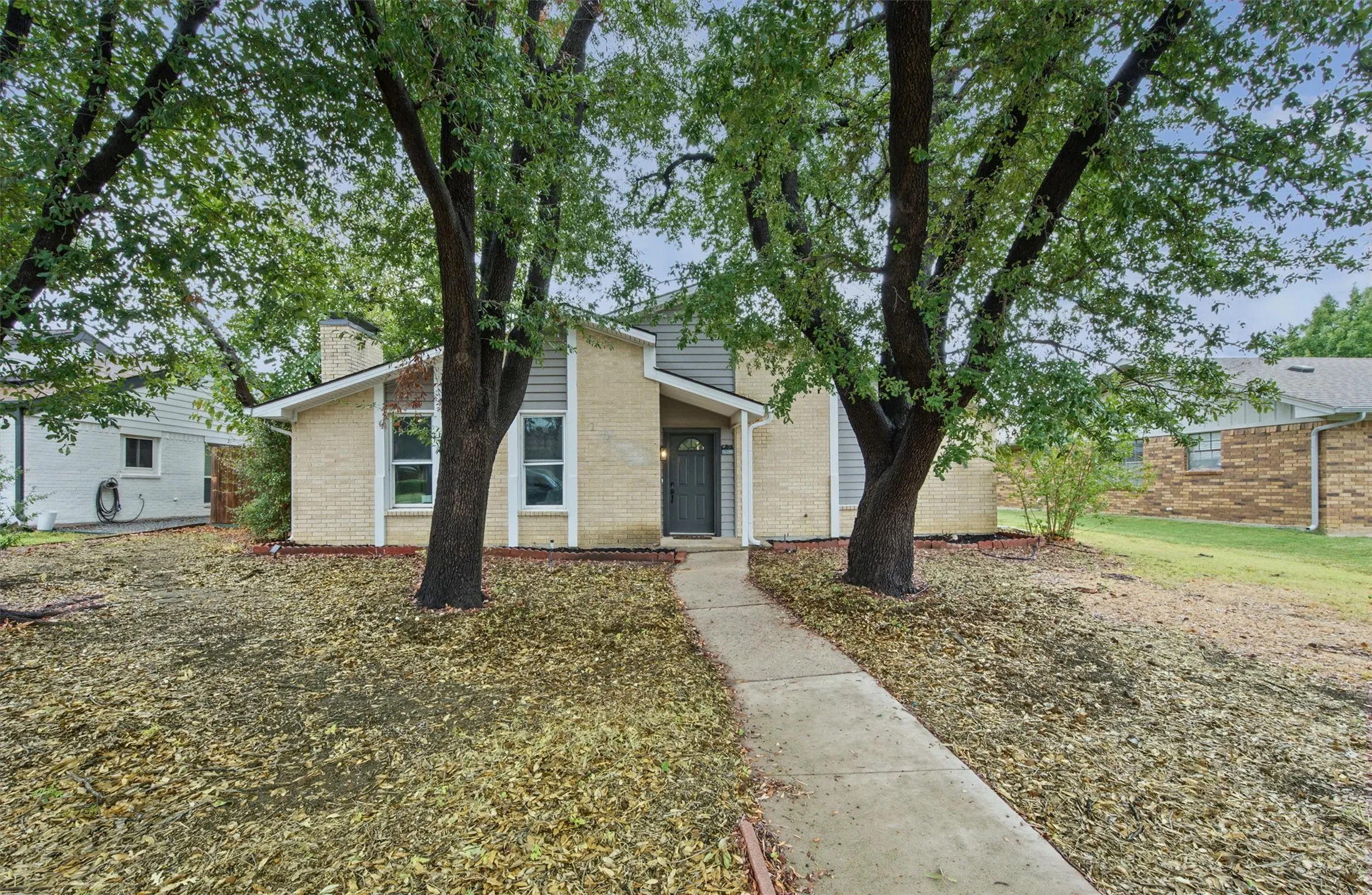 Exterior featuring brick and vertical siding, concrete walkway, and mature trees