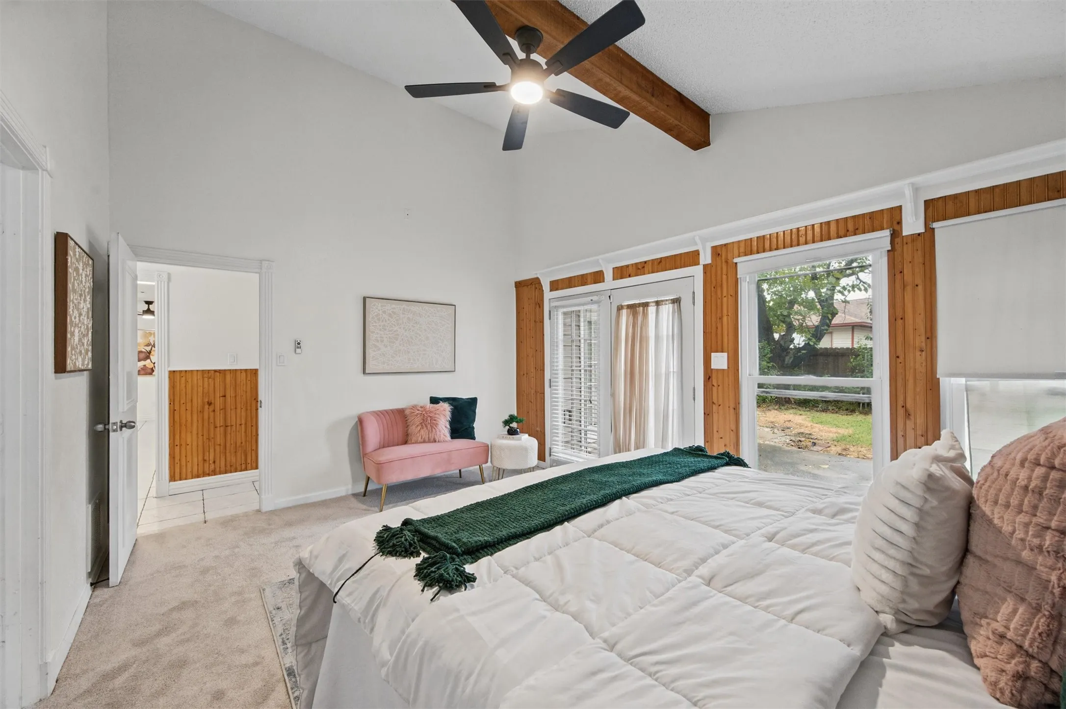 Vaulted ceiling with exposed wood beam, ceiling fan, wood paneling, and French doors