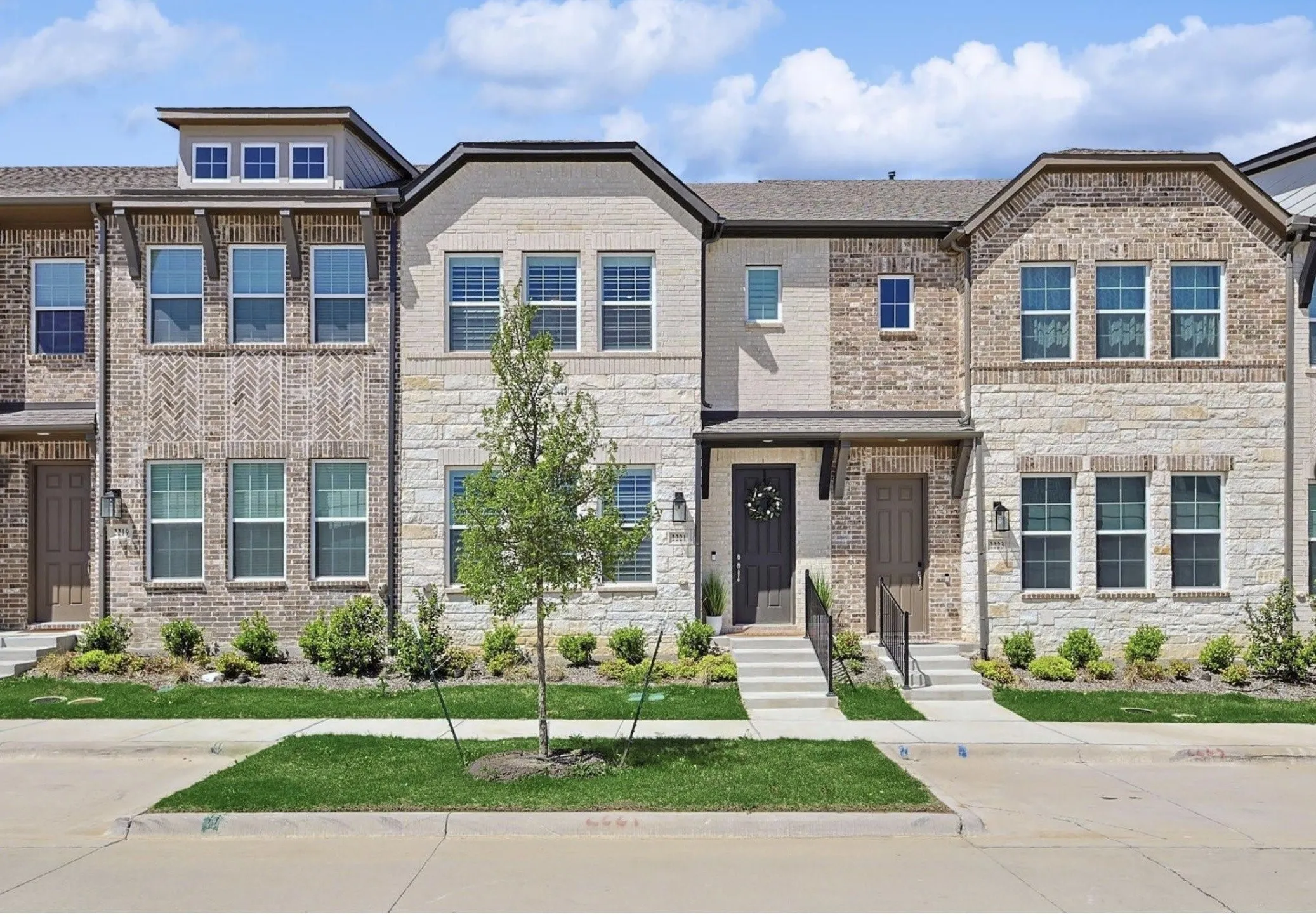 Multi-story townhouse with varied brick and stone exterior, prominent dormer windows, and a covered entryway