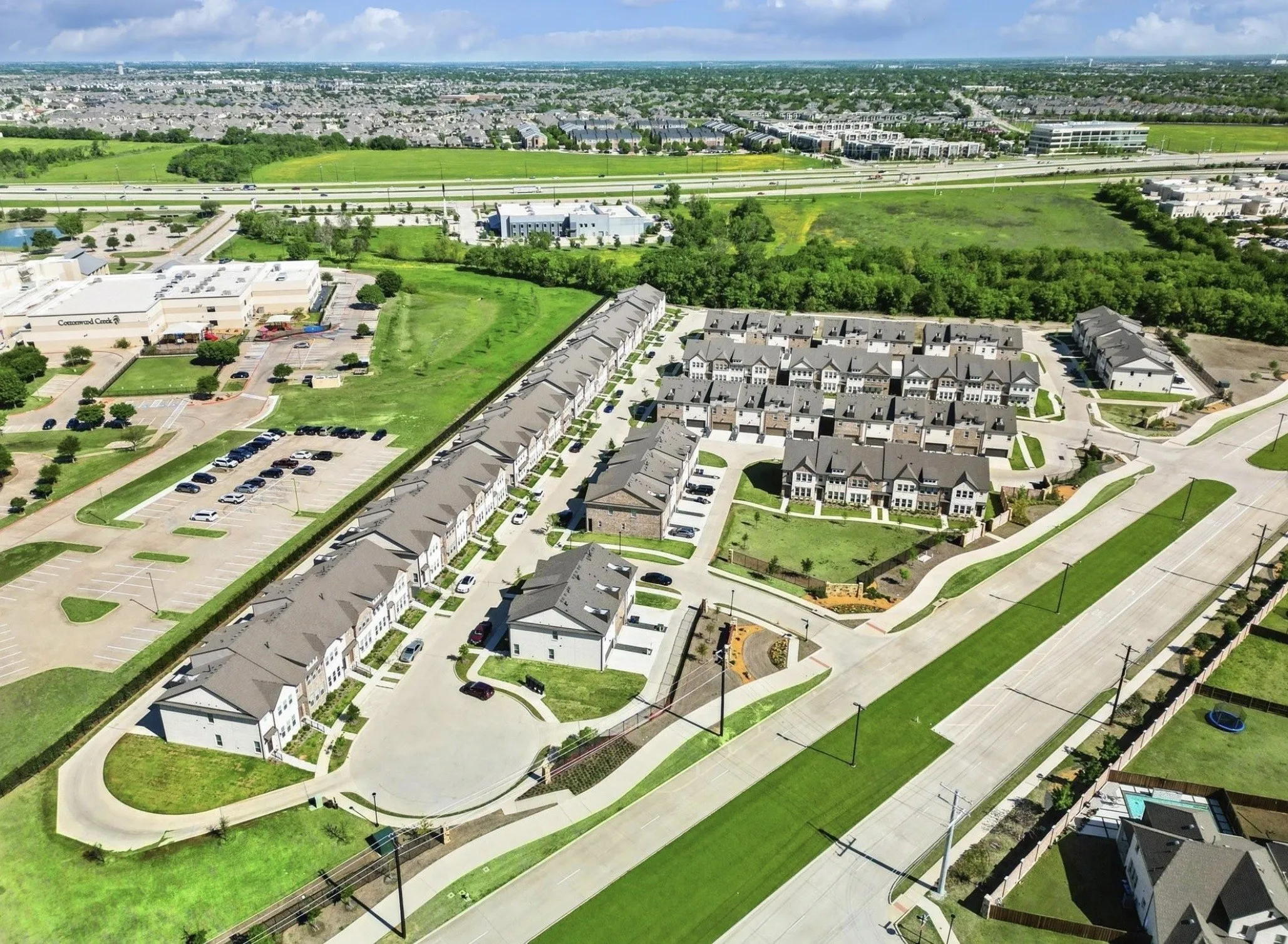 Community with rows of townhomes, green spaces, and paved roads