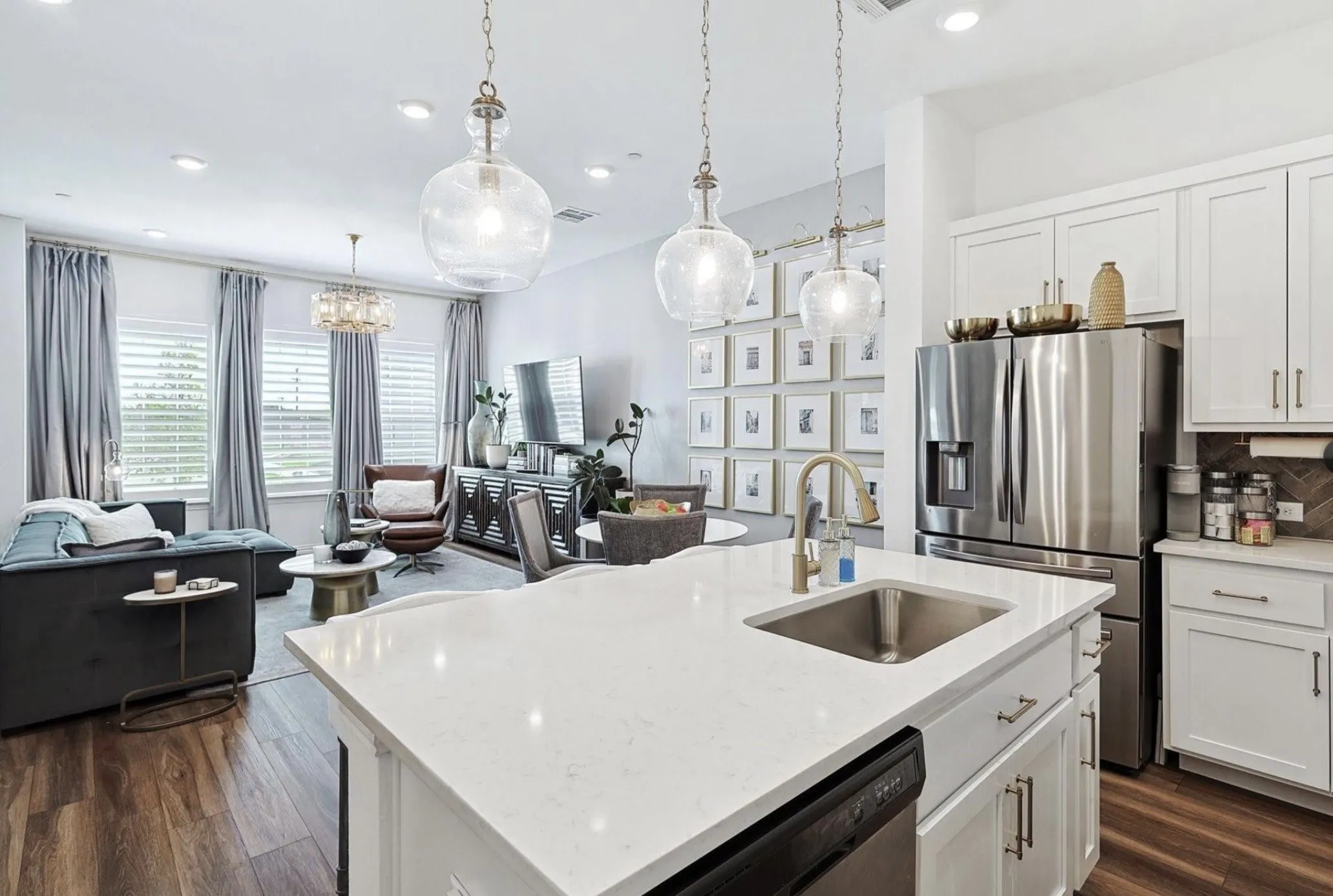 Open-concept living area with wood-finish flooring, white shaker cabinetry, stainless steel appliances, and a kitchen island featuring a sink and white countertop