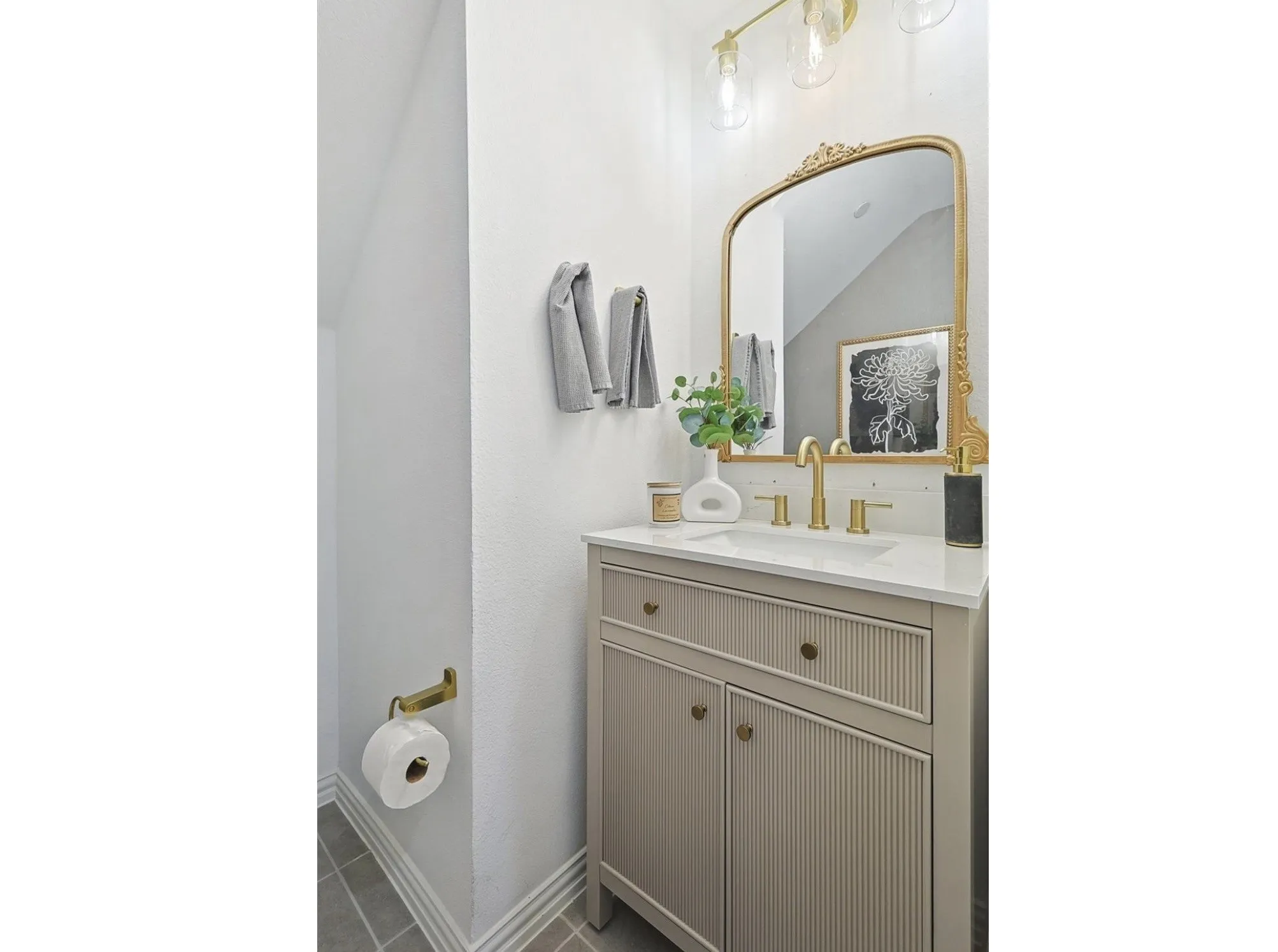 Vanity with integrated sink, gold-finish faucet, and coordinating mirror under a multi-bulb light fixture