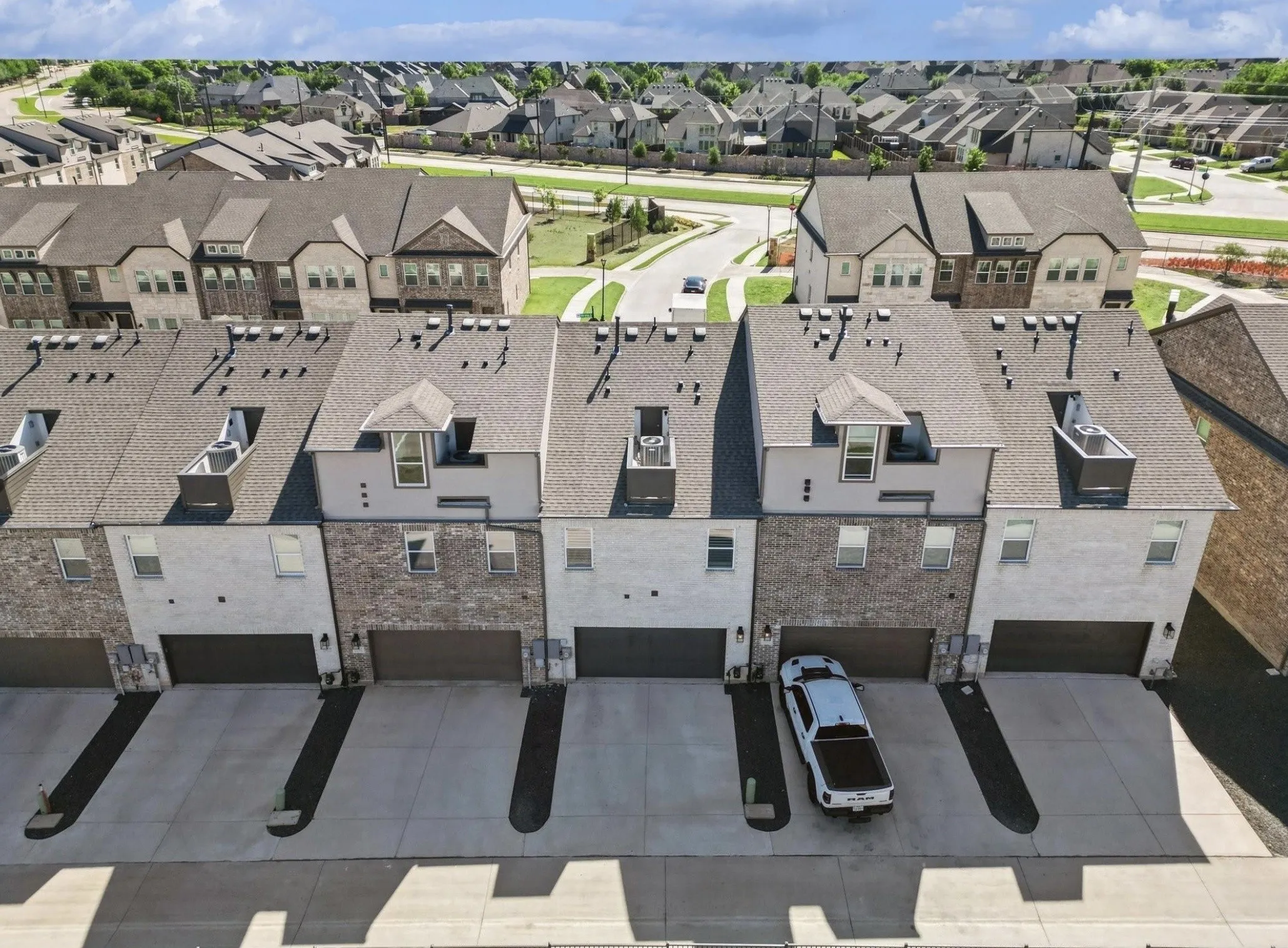 Townhome exterior featuring individual garages, paved driveways, and a mix of brick and stucco finishes