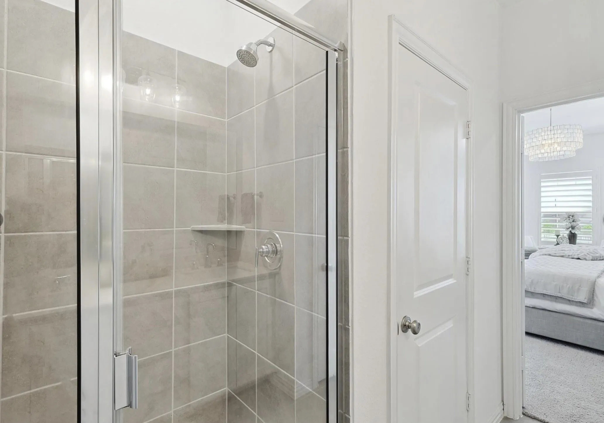 Glass-enclosed shower with gray tiled walls and a chrome showerhead