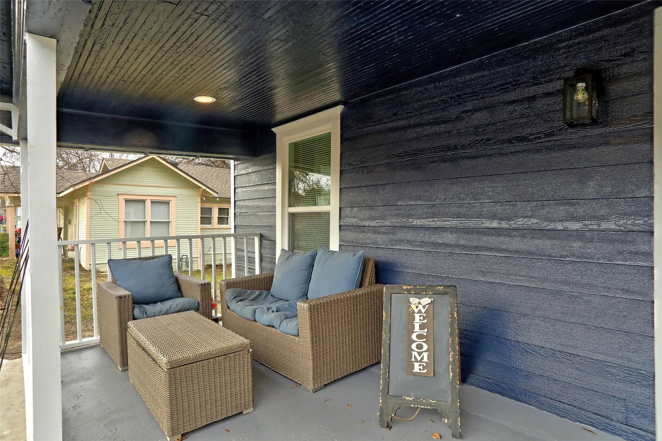 Covered front porch featuring a dark blue wood-finish ceiling, matching wood-finish siding, white railing, and an outdoor wall-mounted light fixture