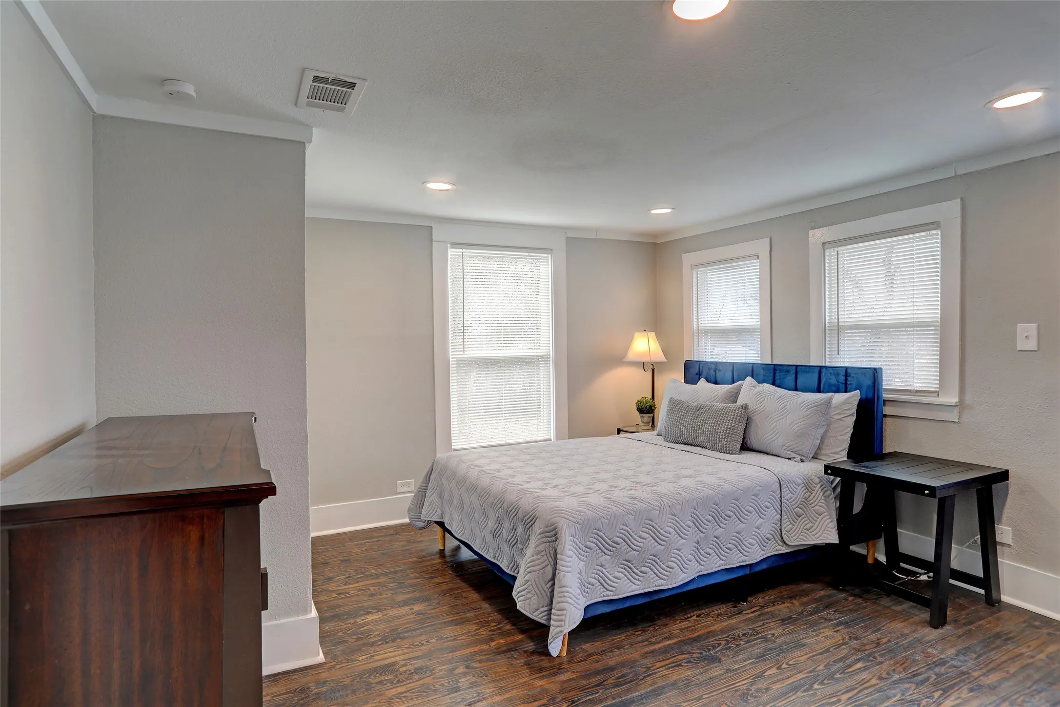 Wood-finish flooring, recessed lighting, crown molding, multiple windows with blinds, and light gray wall paint