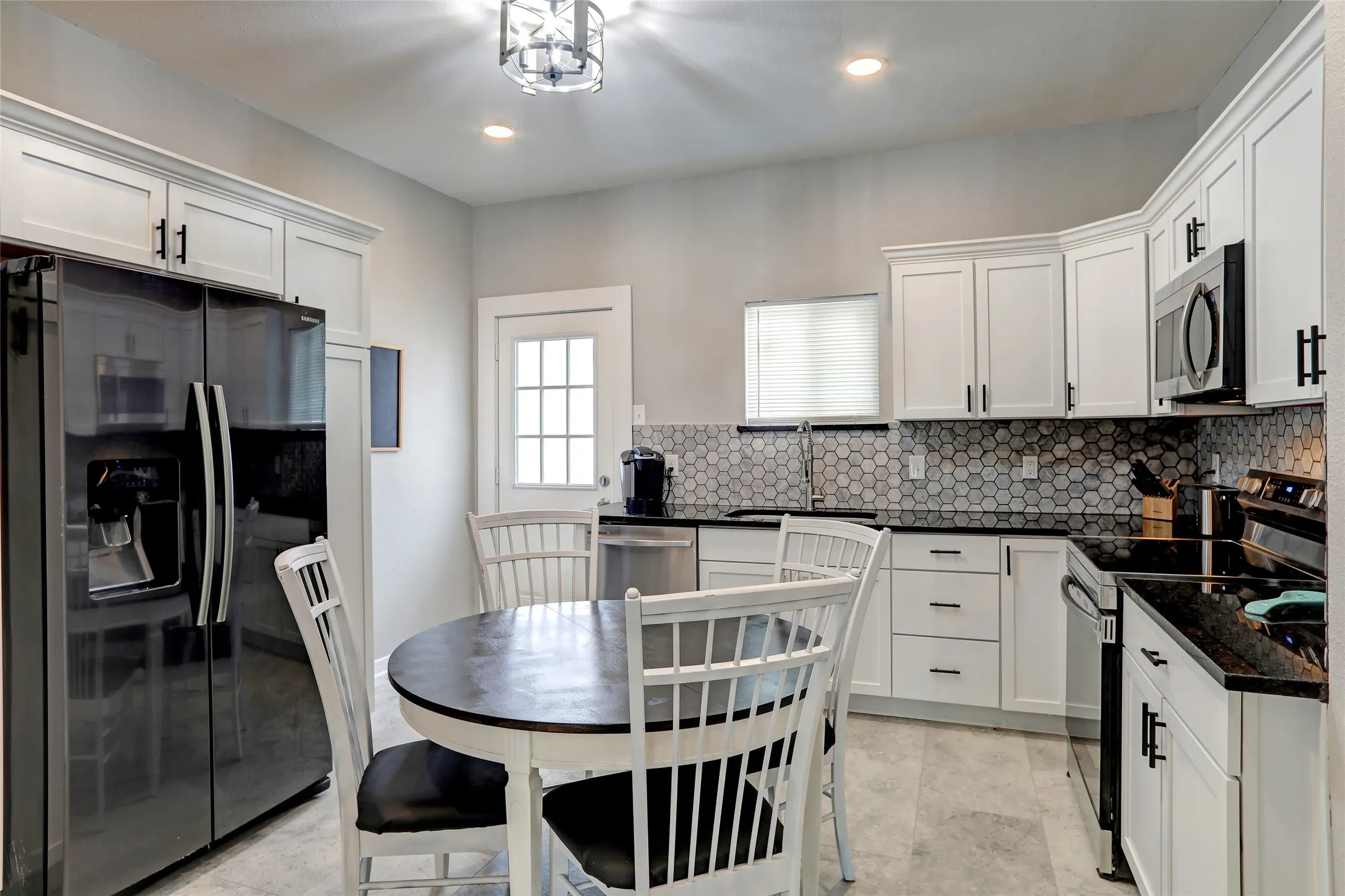 Kitchen featuring white cabinetry, dark countertops, a hexagonal tile backsplash, a black side-by-side refrigerator, and a stainless steel over-the-range microwave