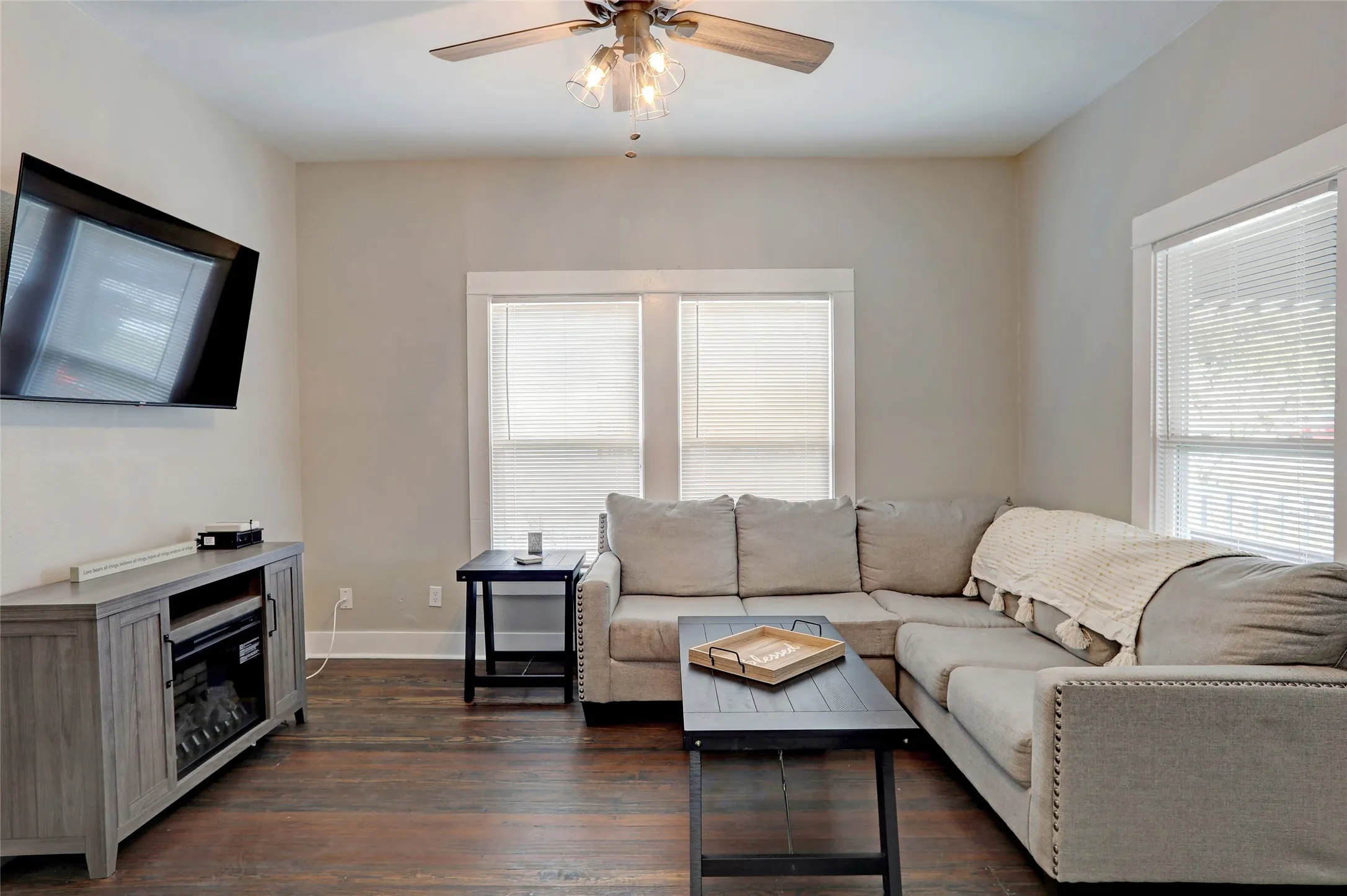 Wood-finish flooring throughout, ceiling fan with integrated lighting, multiple windows with blinds, and neutral painted walls