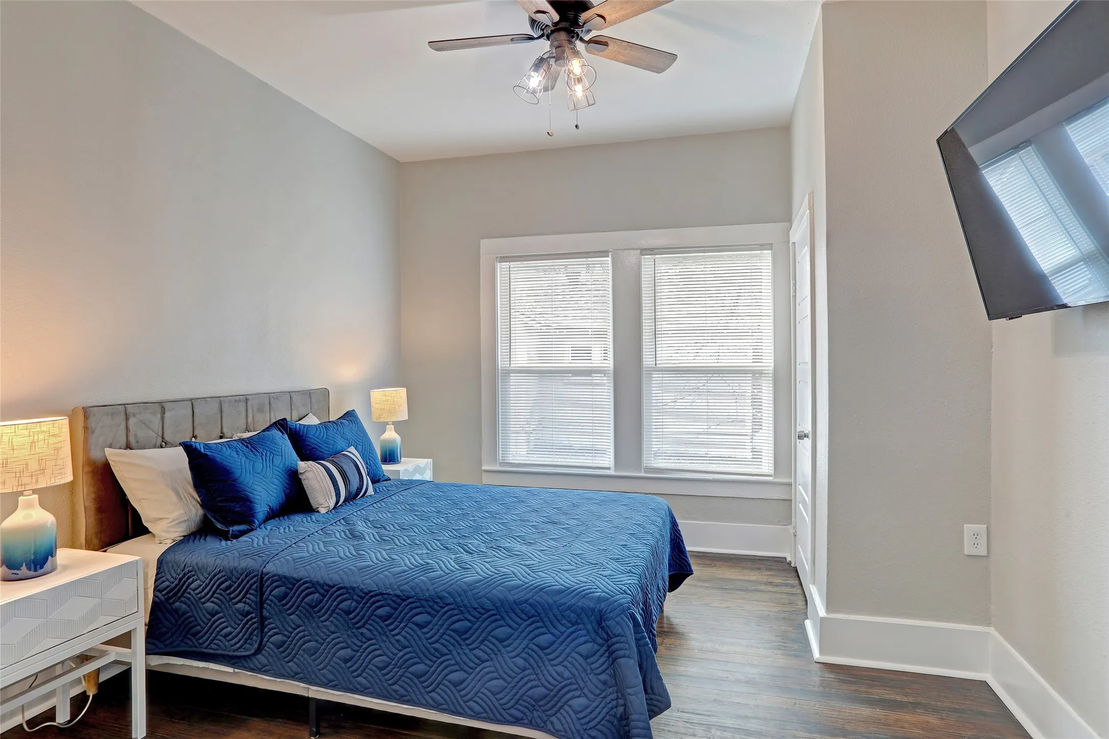 Hardwood-style flooring, ceiling fan, white trim, and two windows with blinds