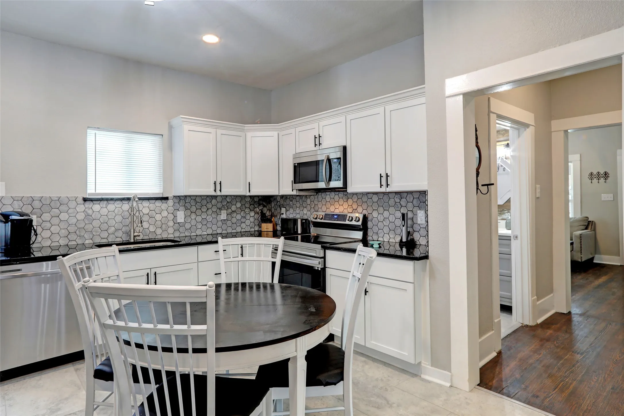 White cabinetry with black hardware, black countertops, stainless steel appliances, hexagonal tile backsplash, and light-colored flooring