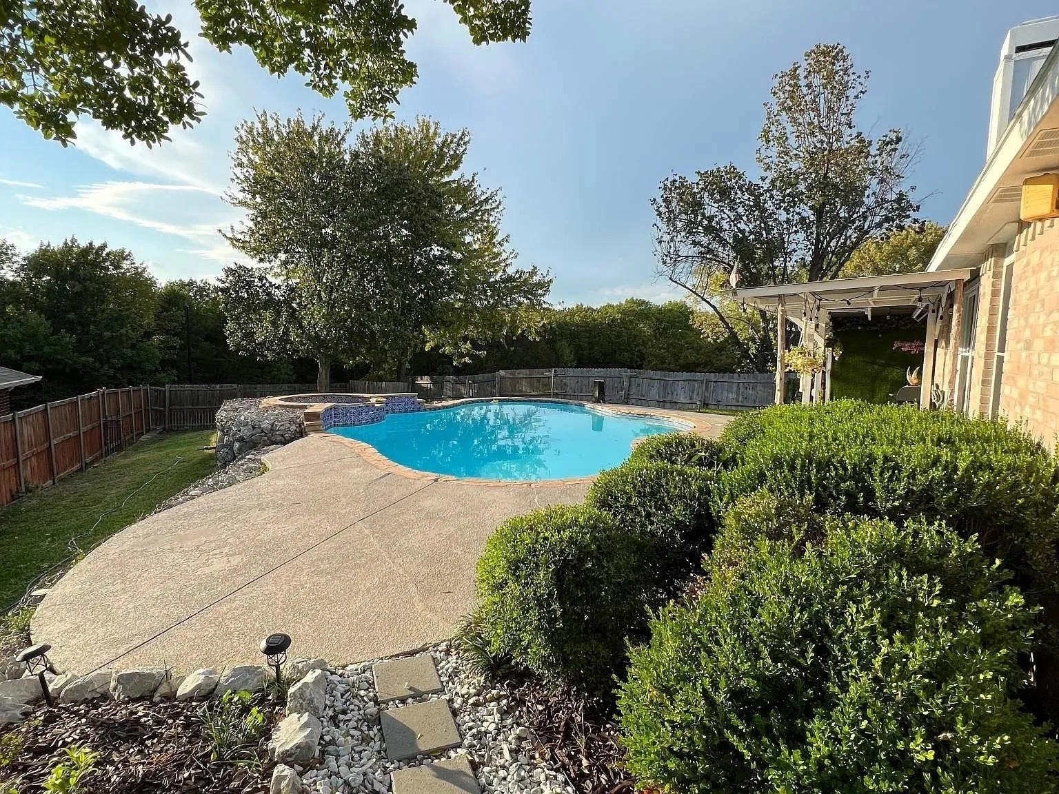 Resort-style backyard featuring a freeform swimming pool, integrated spa with mosaic tile, spacious concrete patio, and mature landscaping