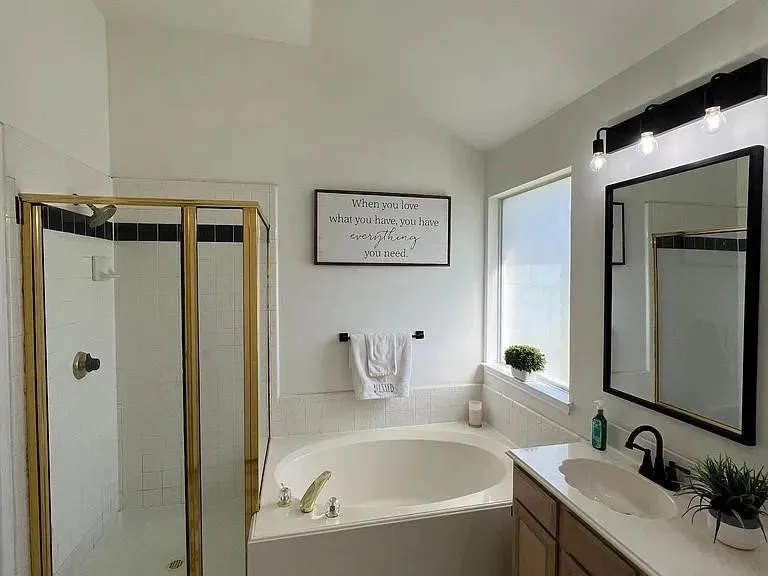 Soaking tub with white tile surround, adjacent to a glass-enclosed shower with brass-finish framing