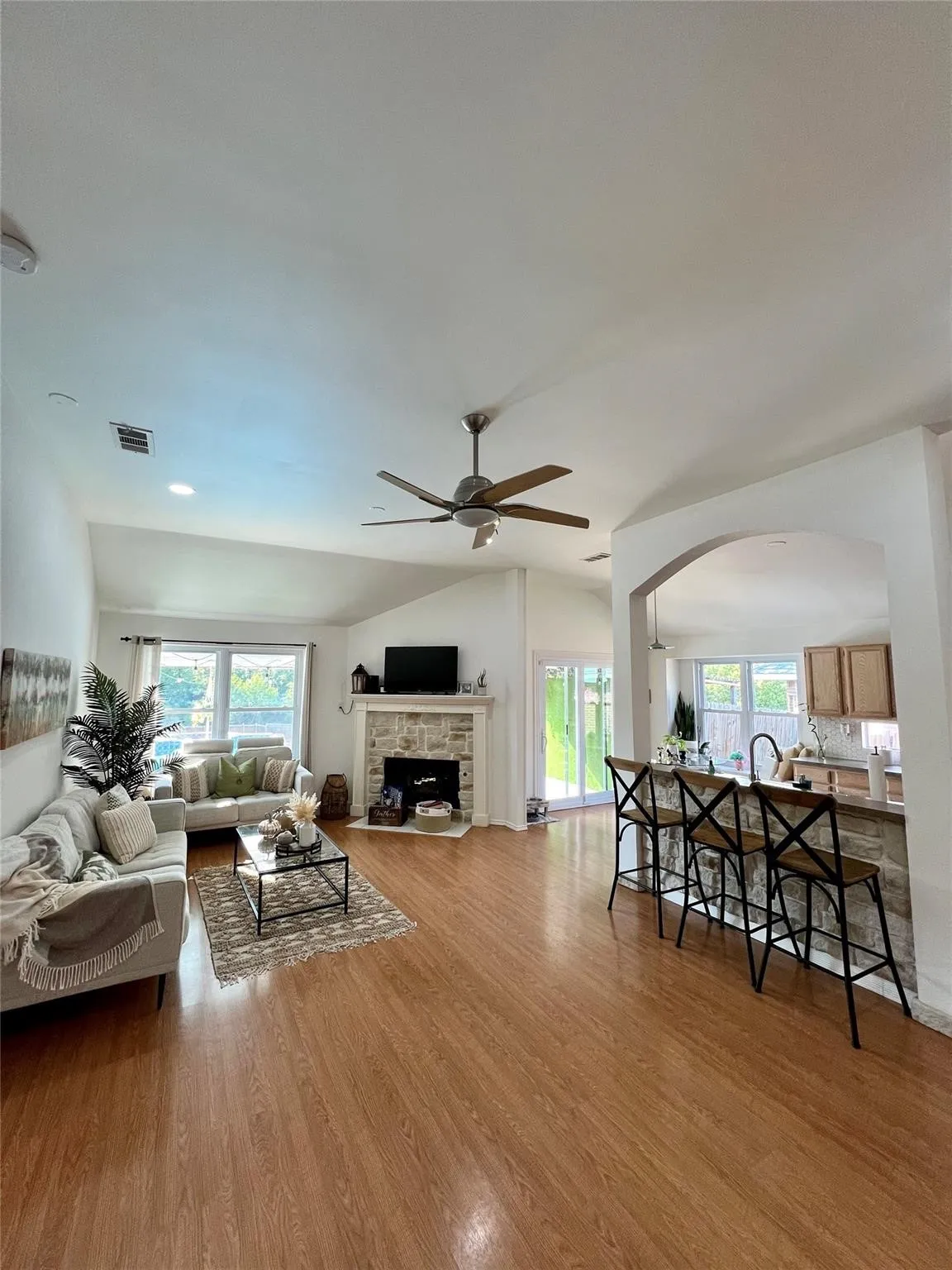 Vaulted ceilings, wood-finish flooring, stone-clad fireplace, kitchen pass-through with breakfast bar, and ceiling fan