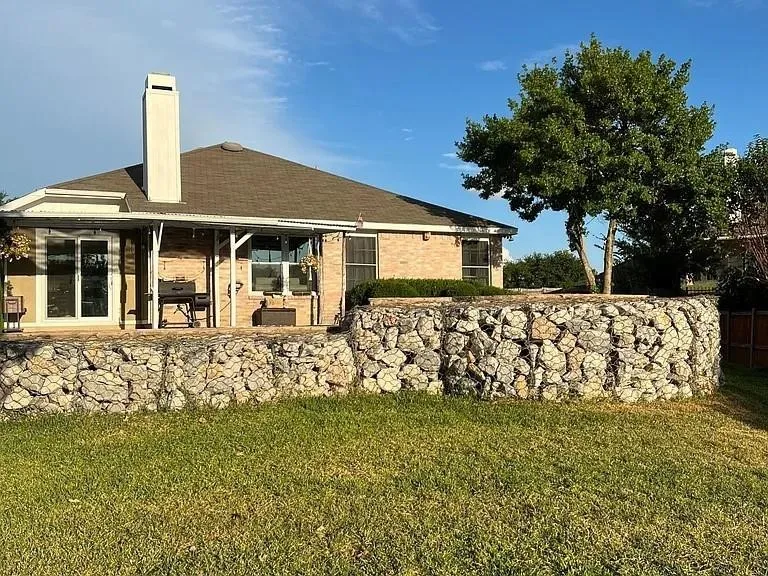 Exterior featuring brick construction, a covered patio, and a gabion retaining wall