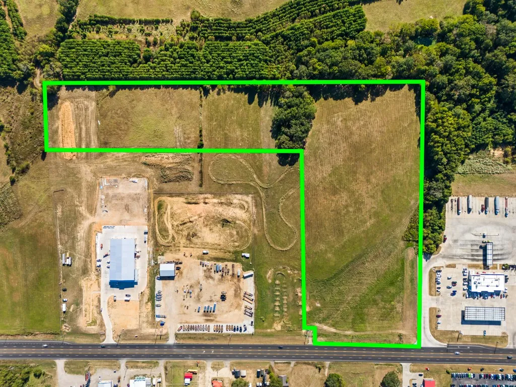 Expansive land parcel featuring open fields, wooded areas, and road frontage