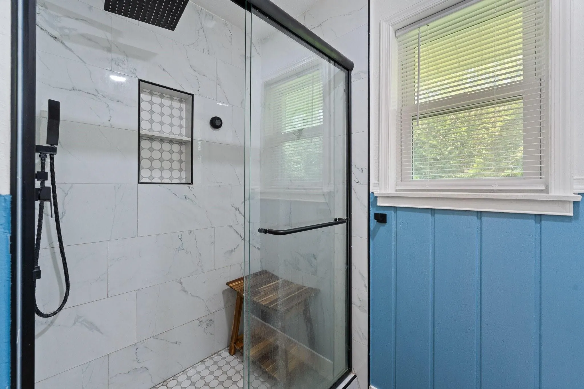 Glass-enclosed shower with a matte black fixture, rainfall showerhead, tiled niche, and mosaic tile flooring