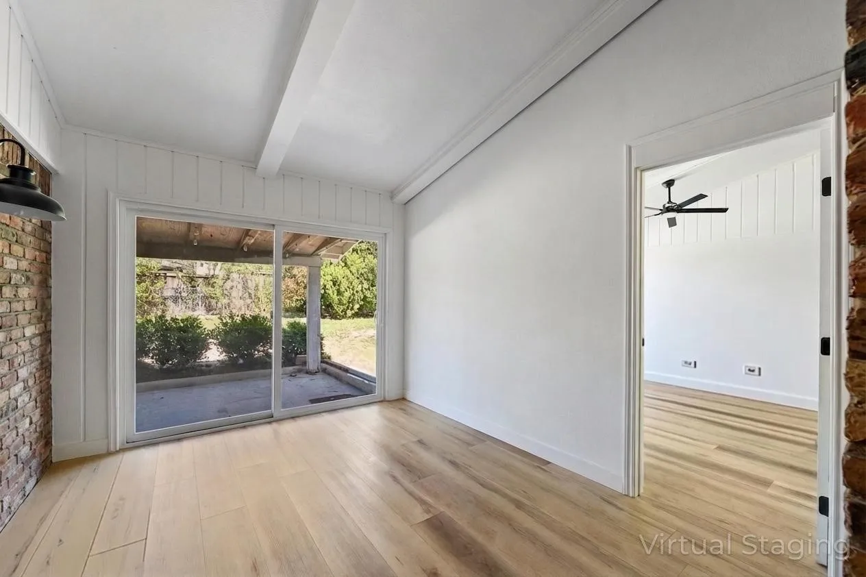 Wood-finish flooring, exposed brick accent wall, white painted wood paneling, white exposed ceiling beams, and a sliding glass door