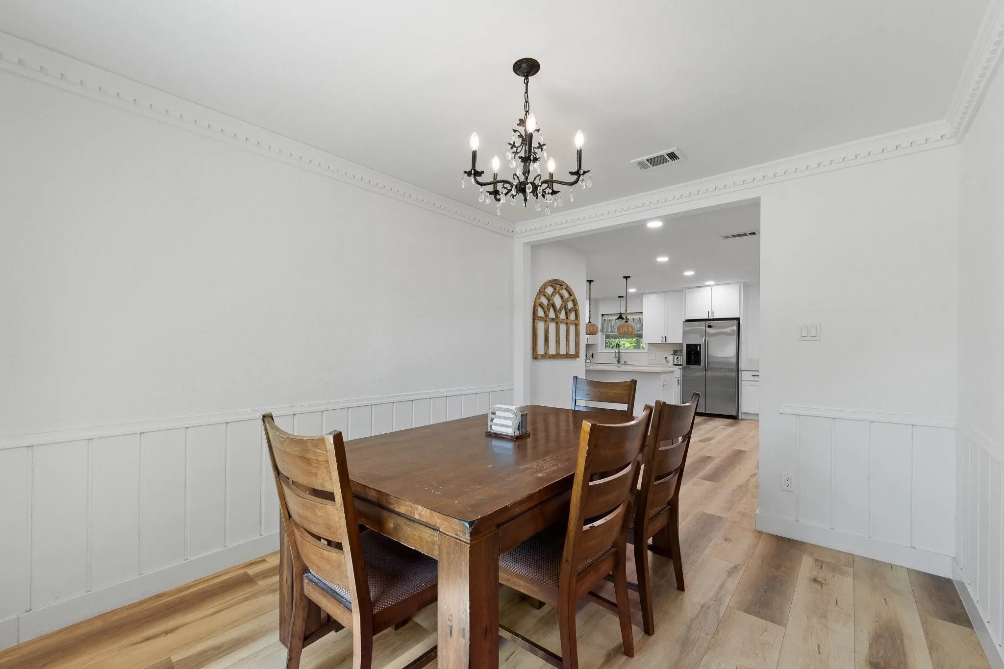 Wood-finish flooring, wainscoting, crown molding, and a chandelier illuminate the dining space