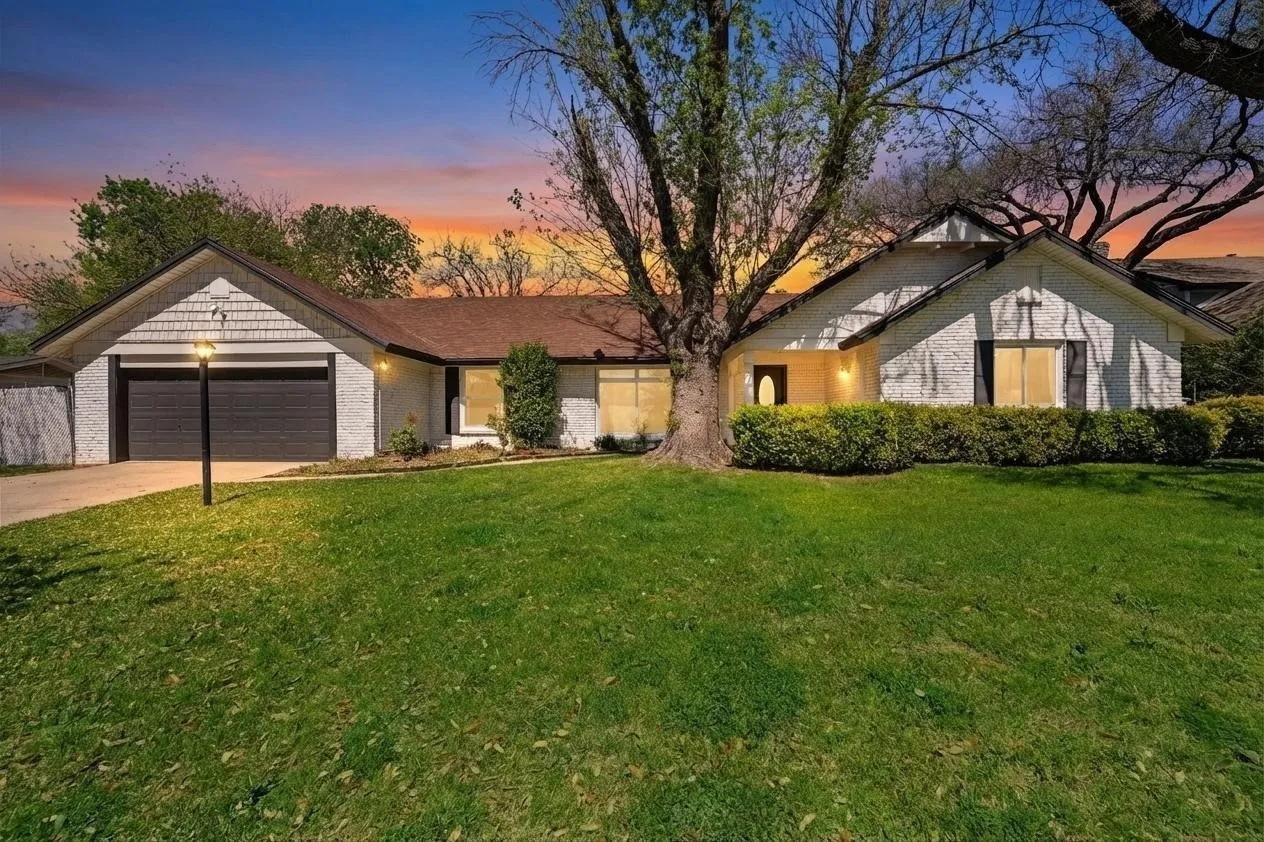 Gable rooflines with shake siding accents, attached two-car garage, manicured shrubbery, and a mature shade tree