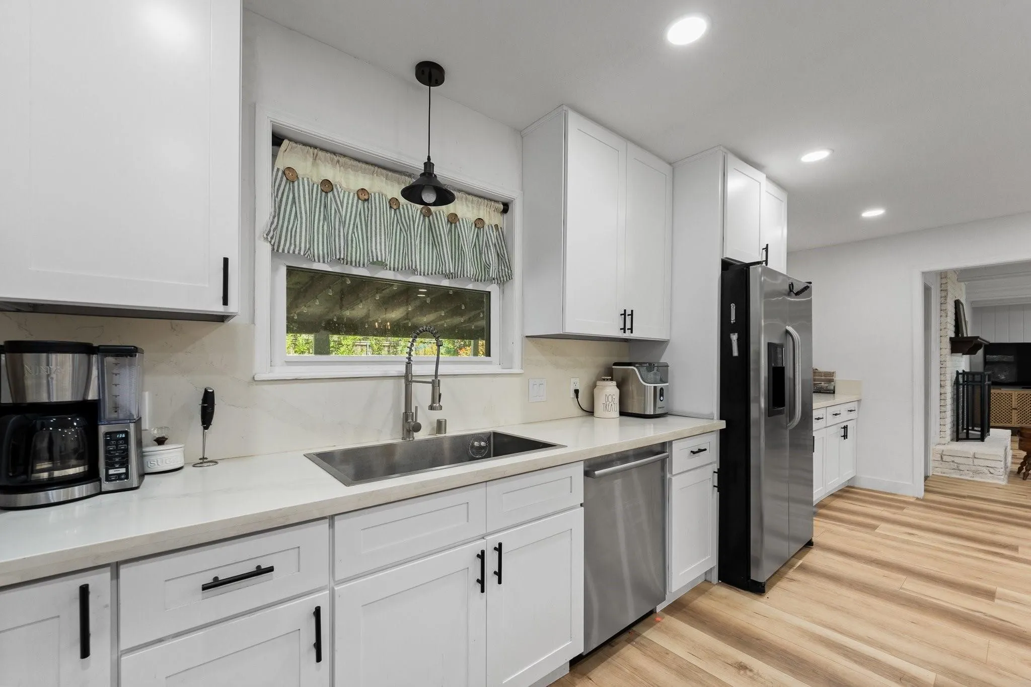White cabinetry with black hardware, light-toned countertops, stainless steel appliances, stainless steel sink with a gooseneck faucet, and wood-finish flooring