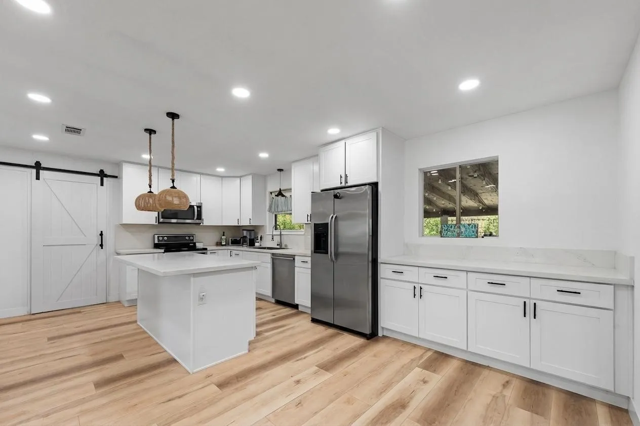 Modern kitchen featuring white cabinetry, light countertops, wood-finish flooring, recessed lighting, and stainless steel appliances