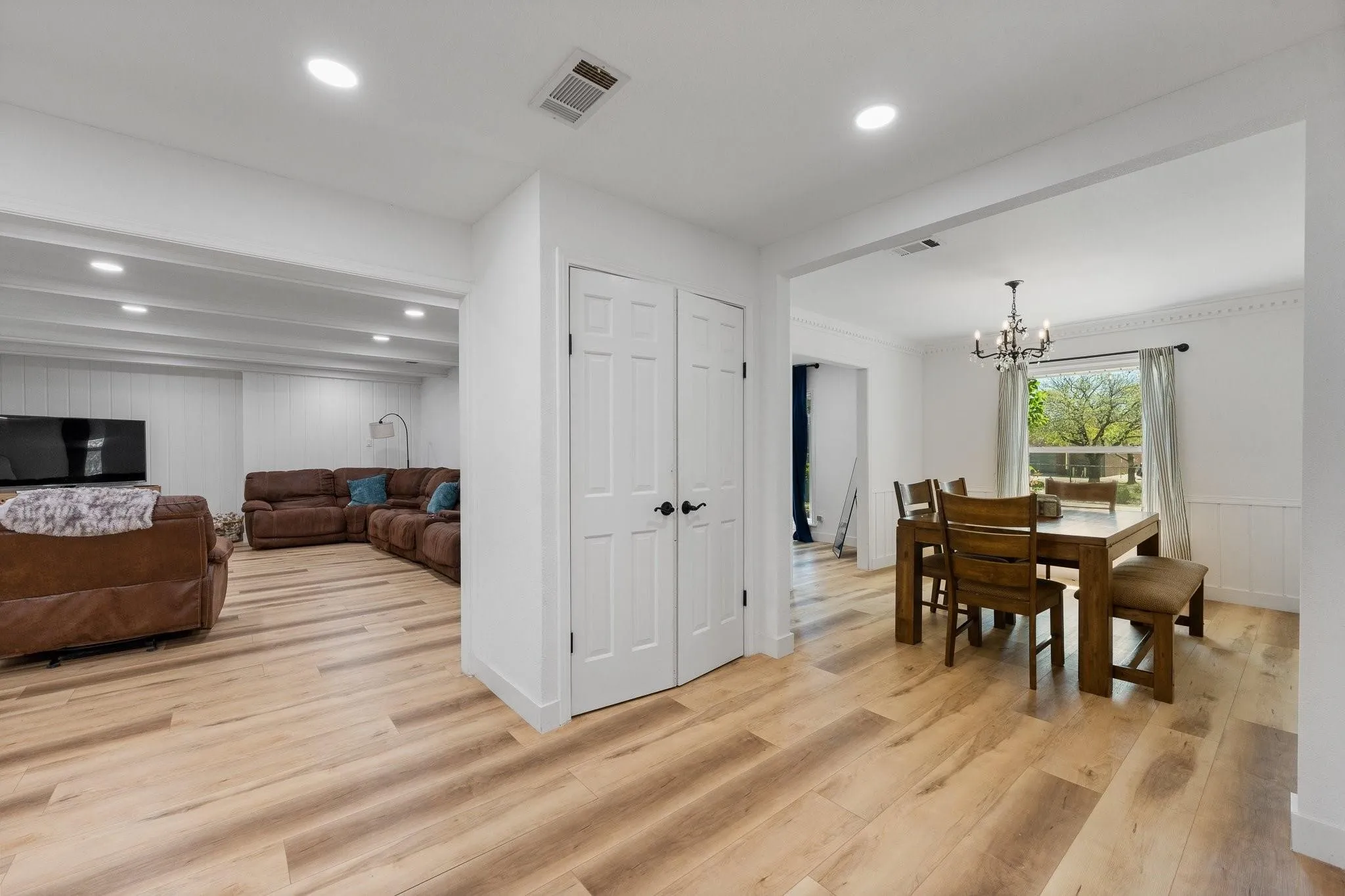 Wood-finish flooring throughout, white paneled walls, recessed lighting, and a dining area with a chandelier