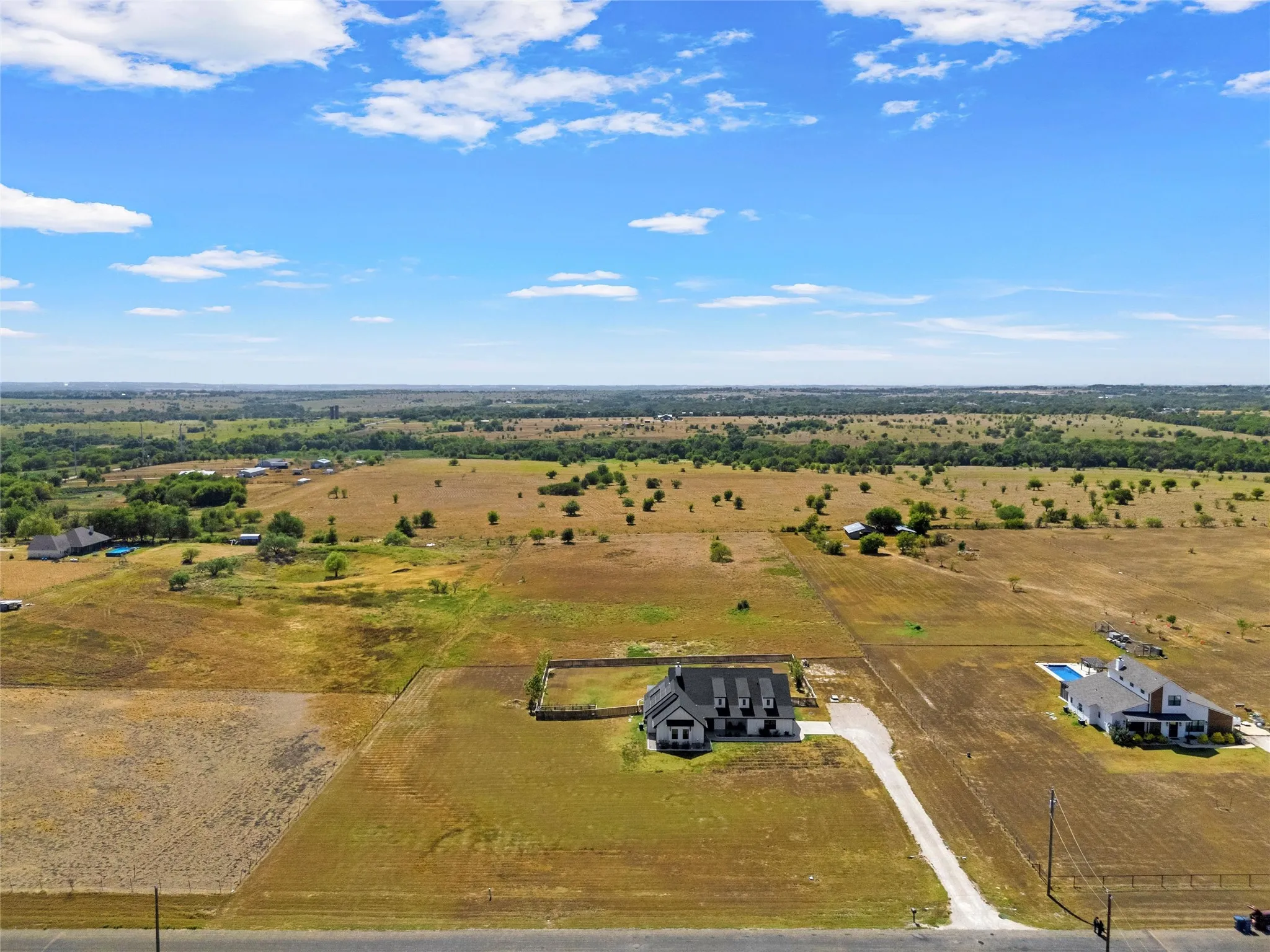 Expansive property featuring a gravel driveway, stone perimeter fencing, and a detached two-story residence with a dark gray roof