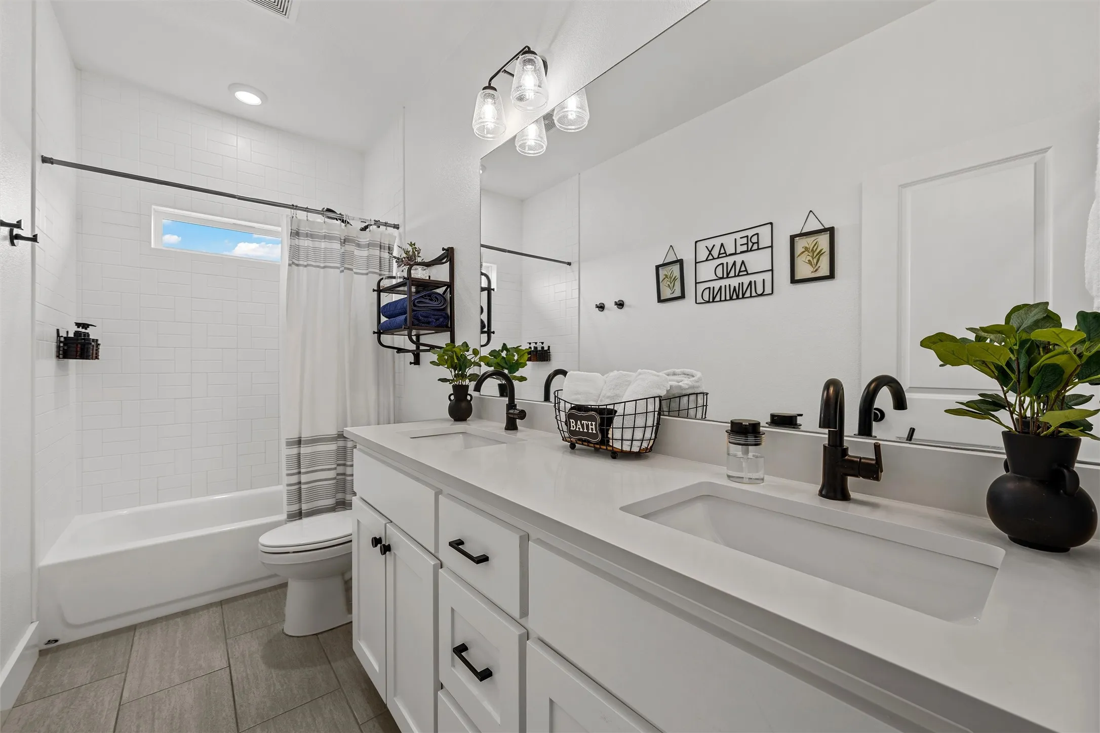 Bathroom featuring a dual vanity, white cabinetry, integrated sinks, black hardware, and a tub with subway tile surround (hall bathroom)