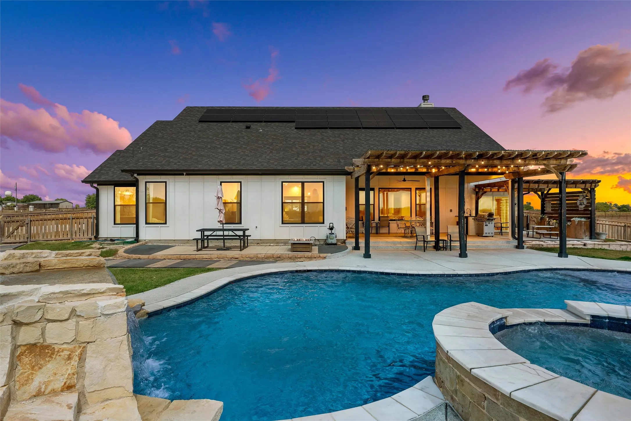 In-ground swimming pool with integrated spa and stone waterfall feature