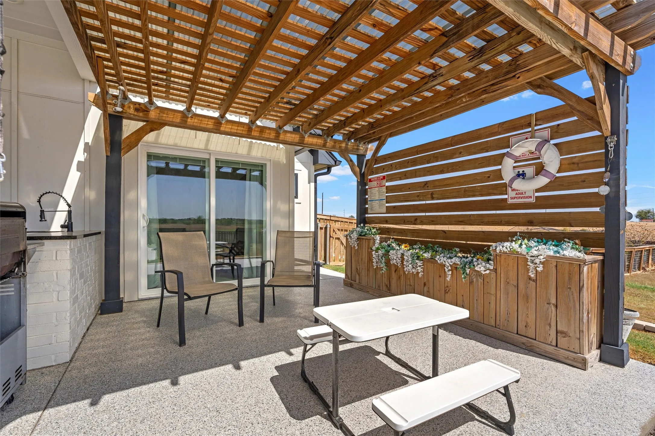 Covered patio featuring a wood pergola, built-in outdoor kitchen with a sink, white brick base, and sliding glass door access