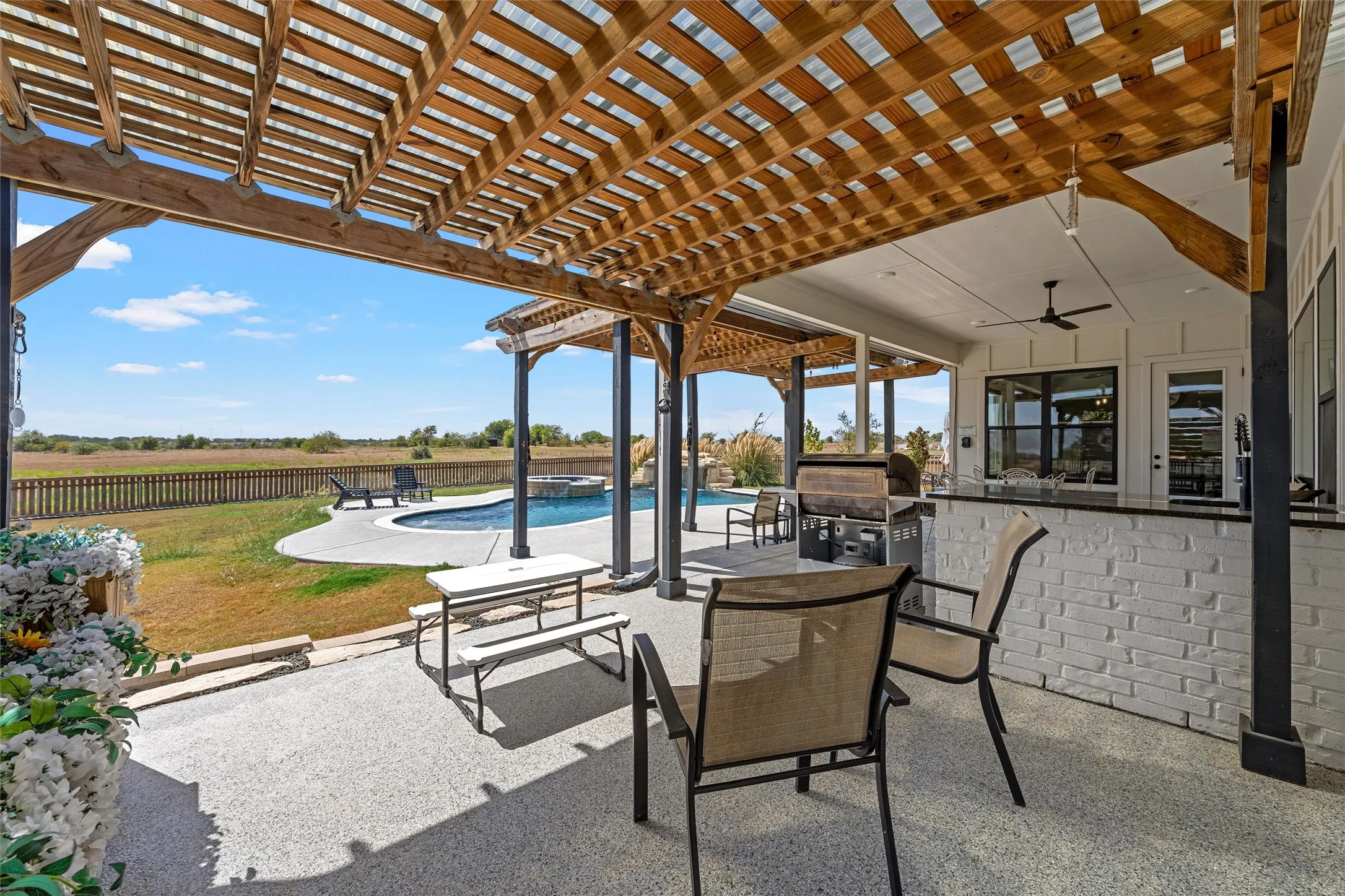 Expansive covered patio with a wood pergola, built-in outdoor kitchen with black countertops, and a swimming pool