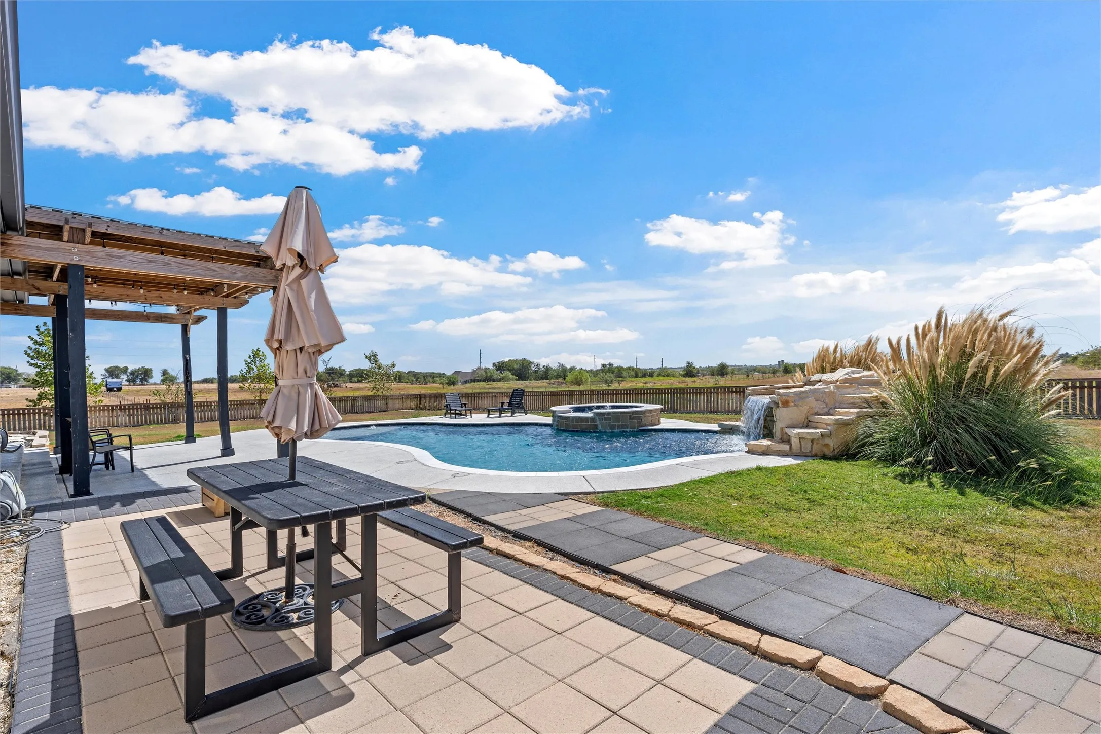 Outdoor swimming pool with integrated spa, rock waterfall feature, paver patio, and an overhead pergola